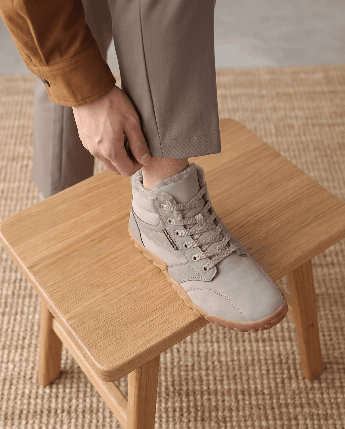 Close view of a hand lacing a beige boot propped on a pale wooden bench
