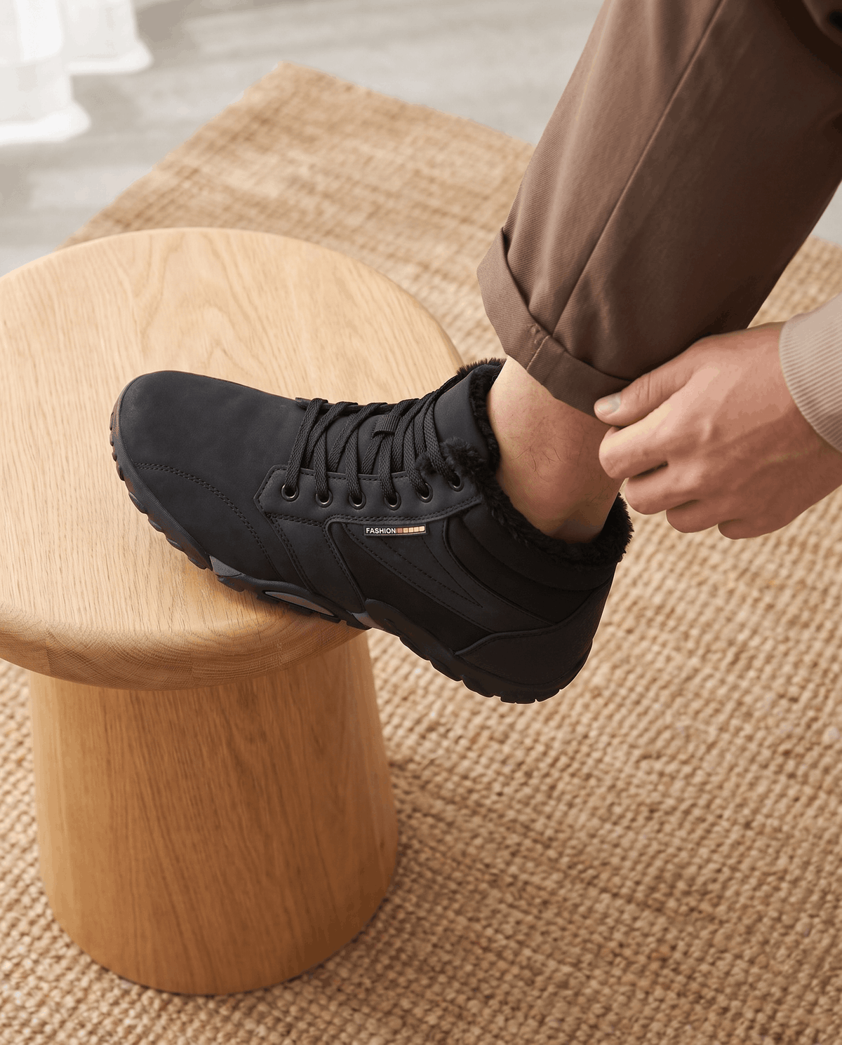 Hands tightening the laces of a black boot resting on a round wooden stool