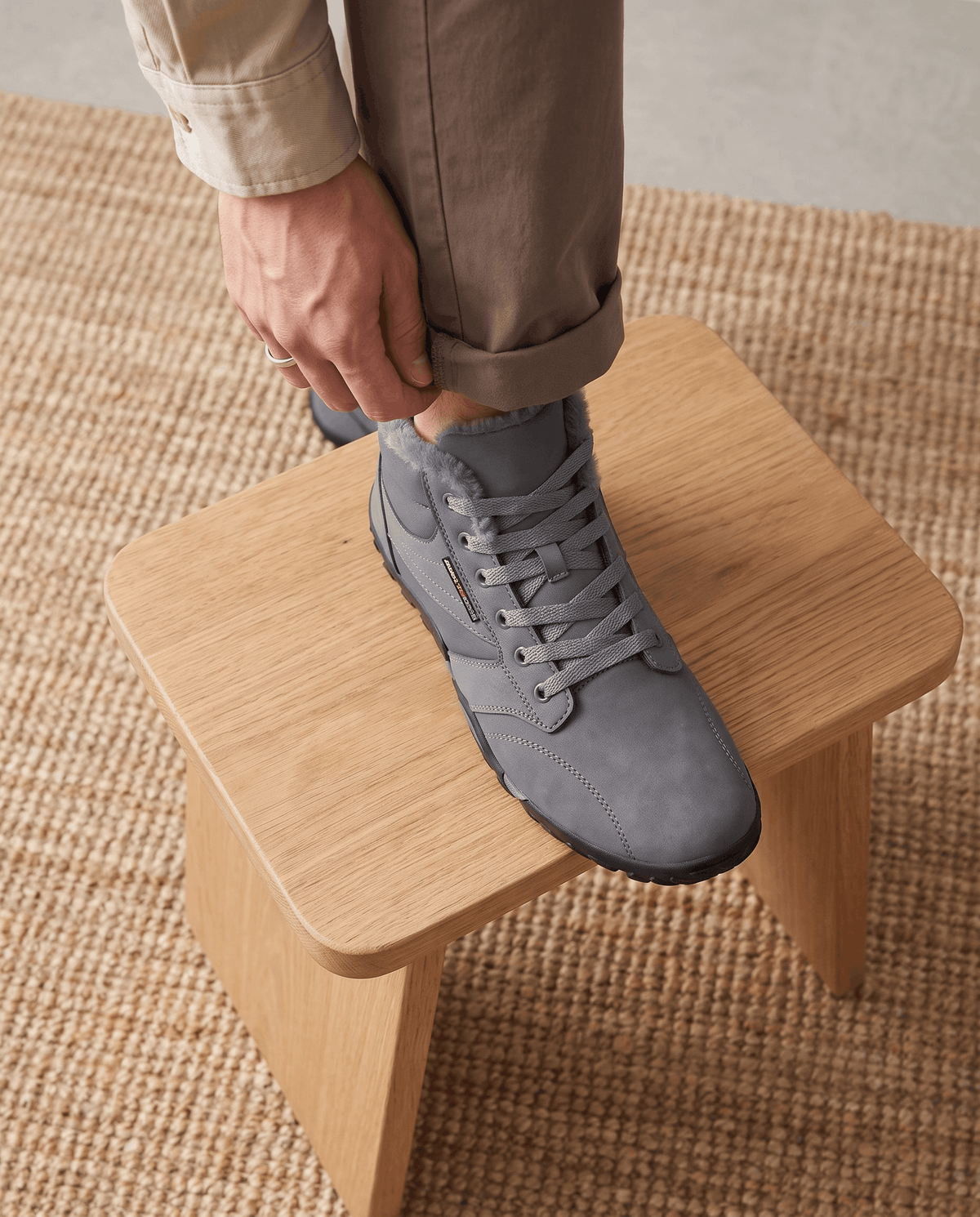 Hands pulling the laces of a gray boot set on a light oak bench