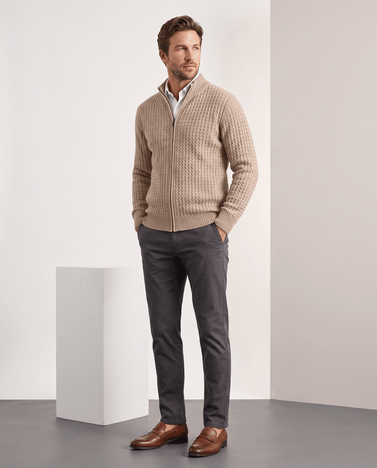 Full-length view of a man wearing the Julian beige cardigan with gray trousers