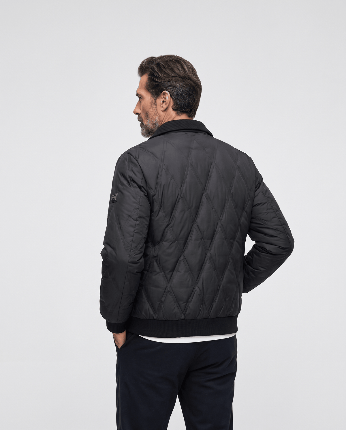 Back view of a man wearing a black diamond quilted puffer jacket with ribbed hem