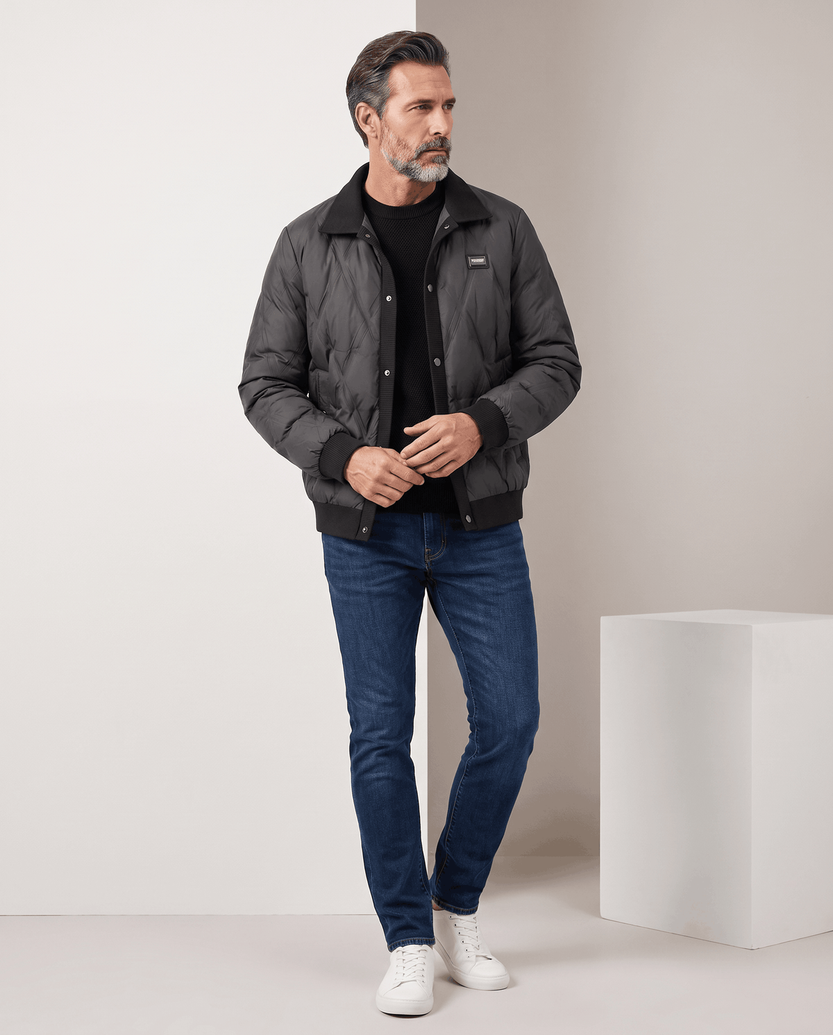 Man standing in a black diamond quilted puffer jacket with blue jeans, full-length view