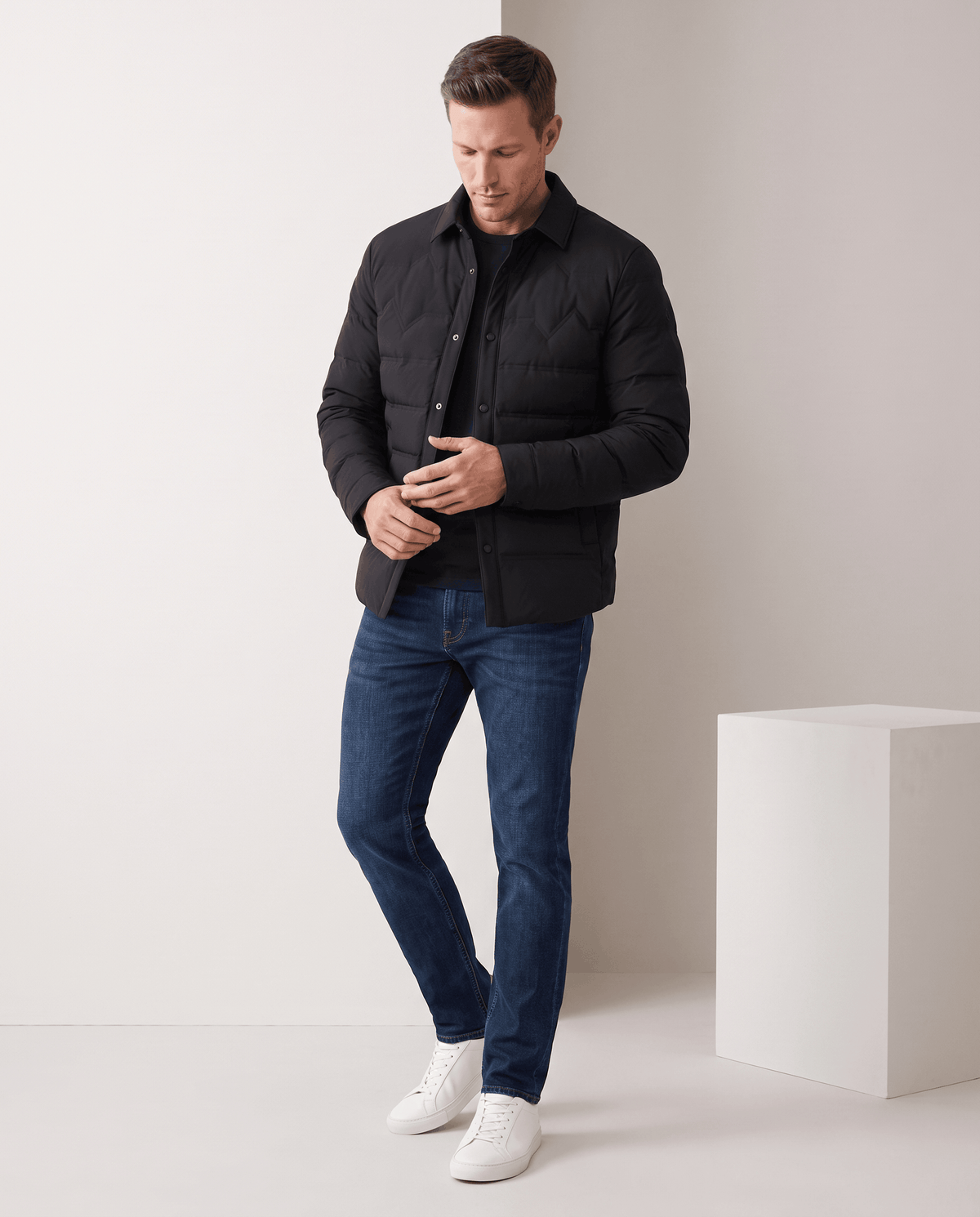 Man standing in a black quilted puffer jacket with blue jeans, full-length view