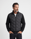 Man wearing a black hybrid puffer jacket with quilted body and fleece sleeves, front view