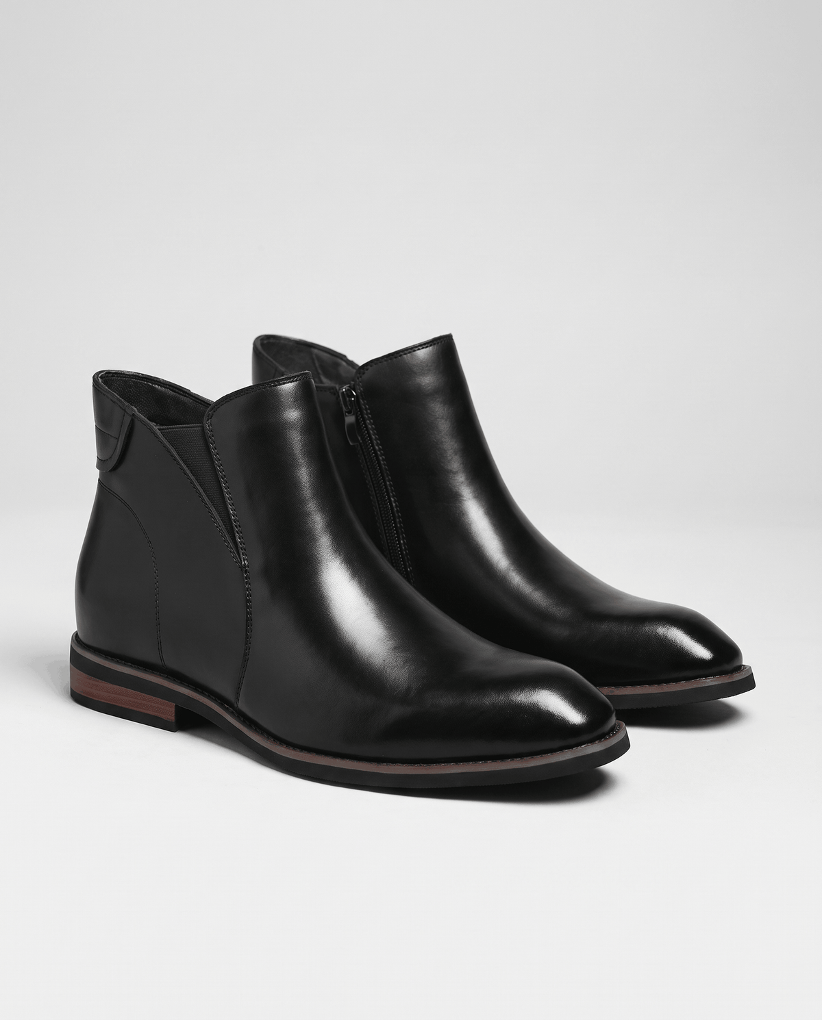 Pair of black Chelsea boots with side zip and low heel on a light floor