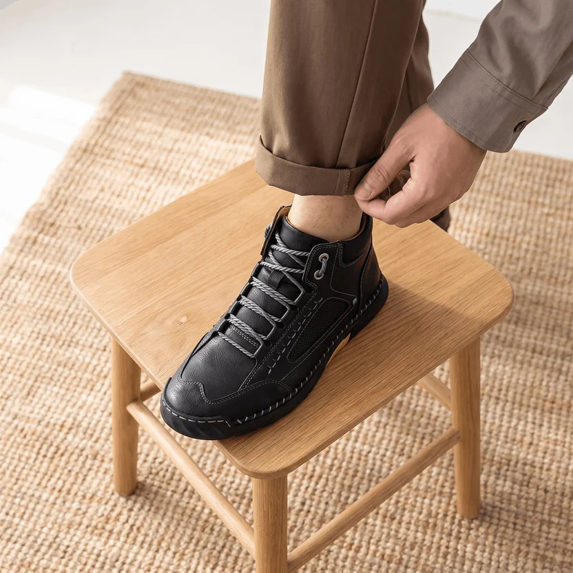 Man lacing a black wide toe box hiking boot with his foot on a wooden stool