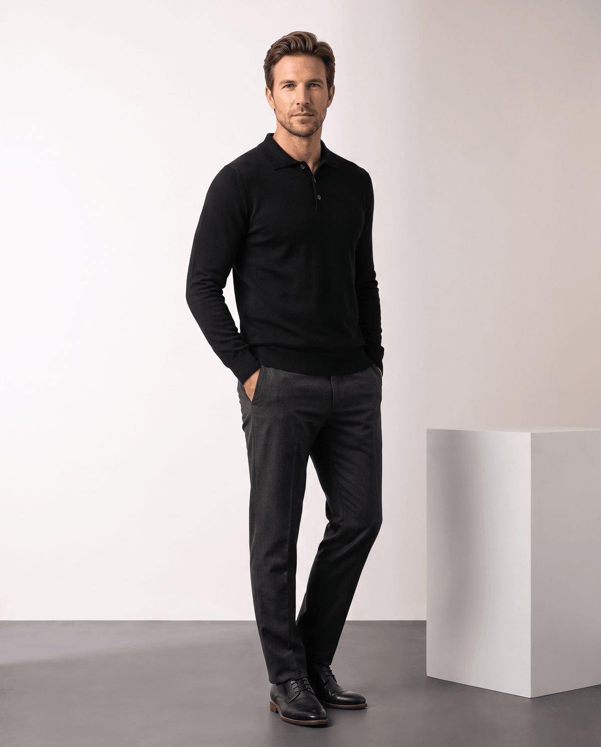 Full-length view of a man wearing the Elias black polo sweater with gray trousers