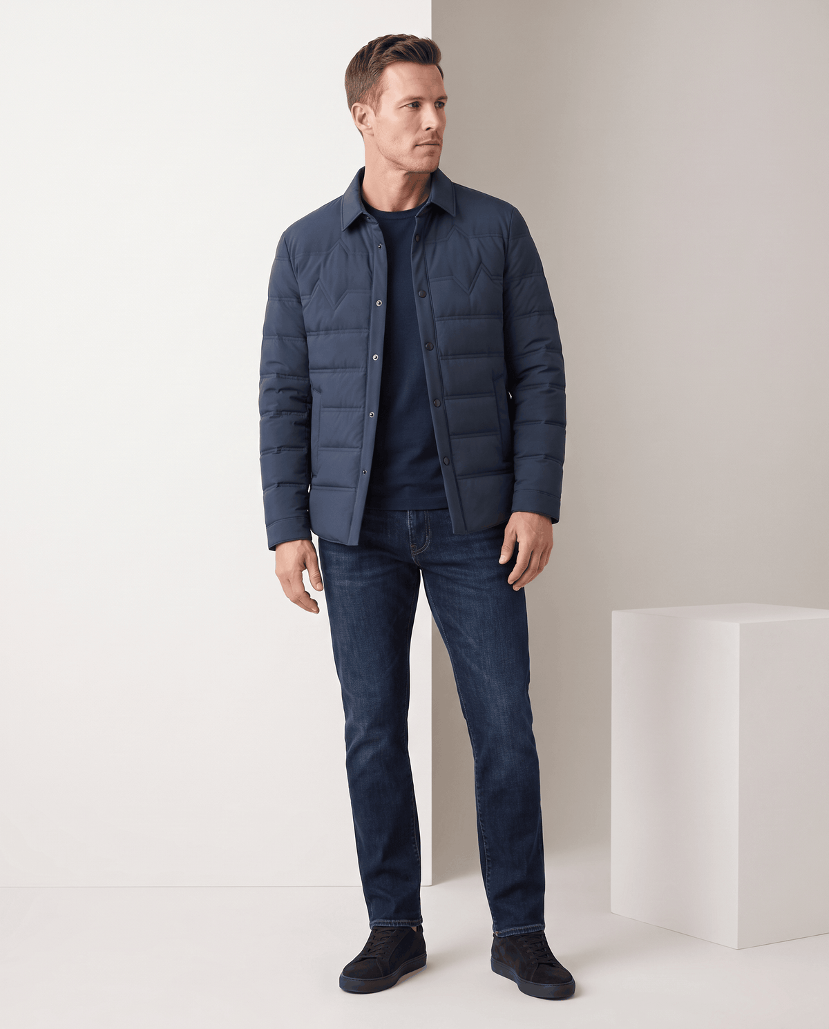 Man standing in a blue quilted puffer jacket with blue jeans, full-length view