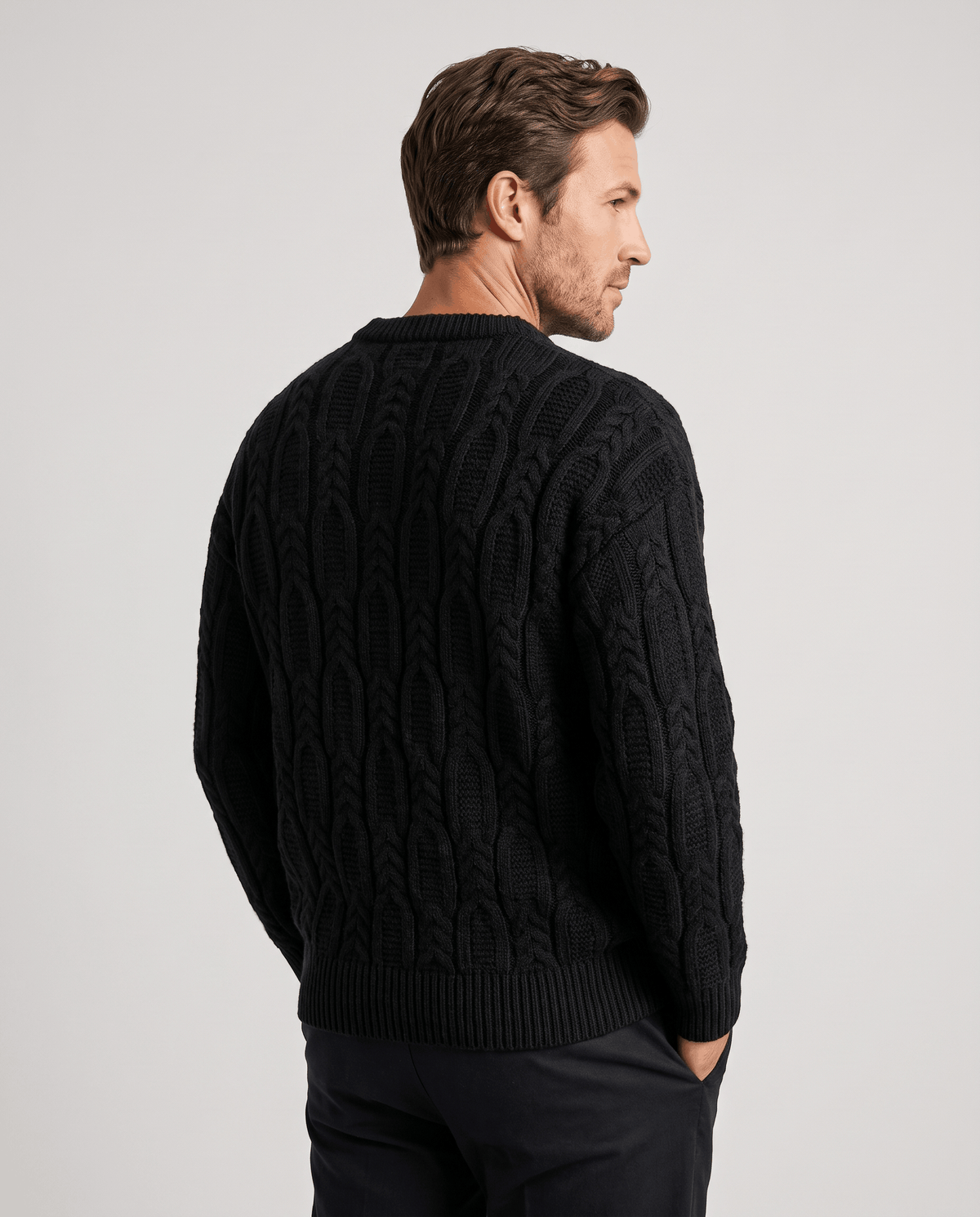 Back view of black cable pullover with hand in trouser pocket