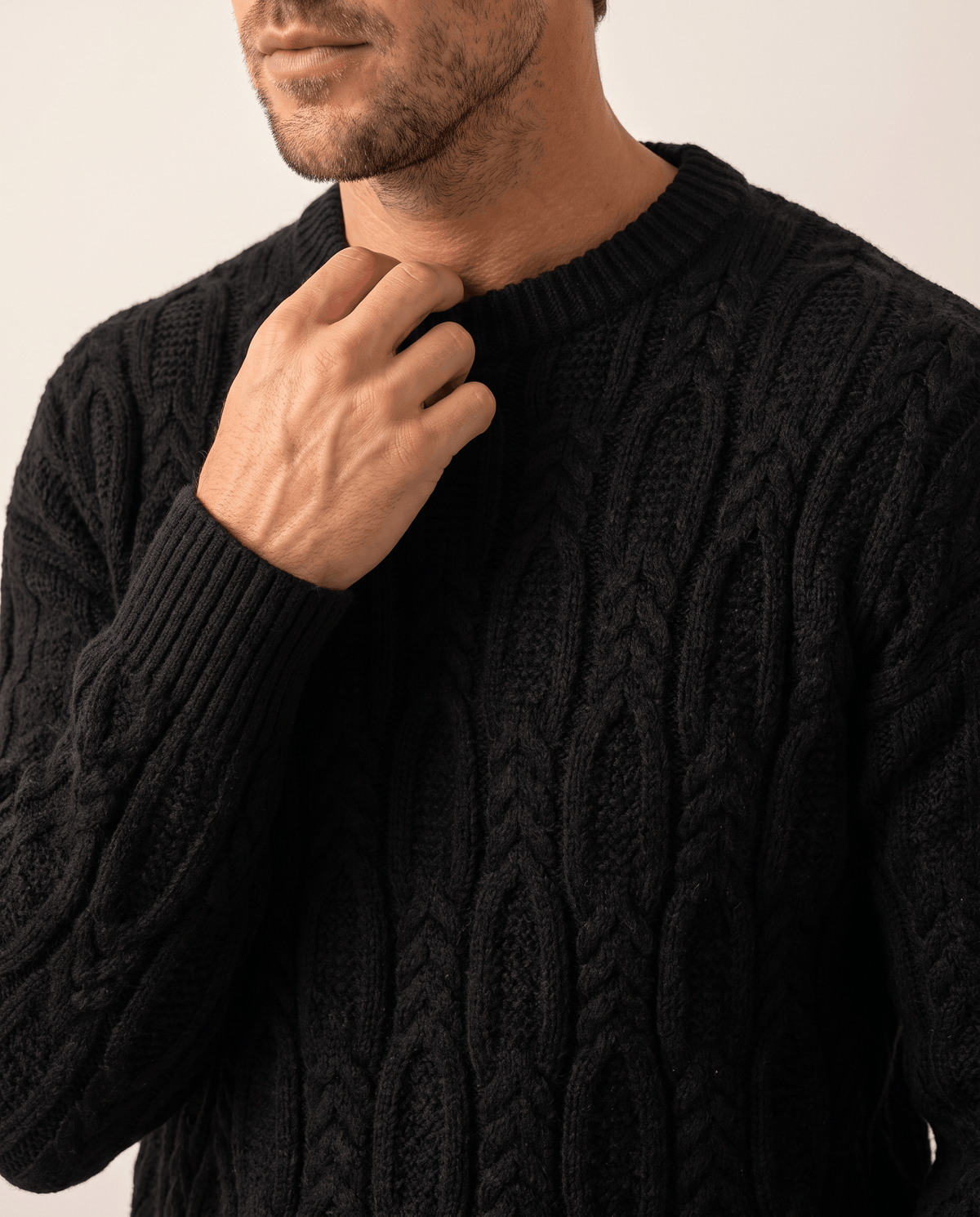 Man touching the ribbed crew collar of a black cable sweater