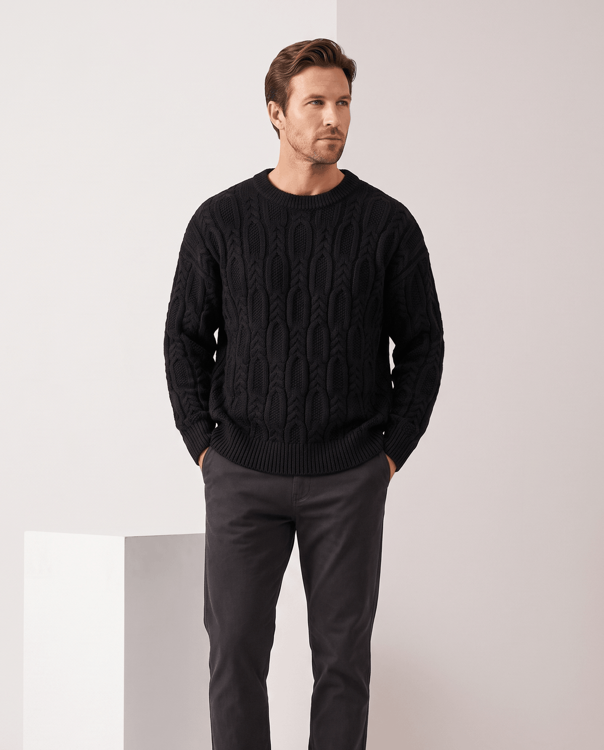 Model in black crew neck cable sweater with charcoal trousers