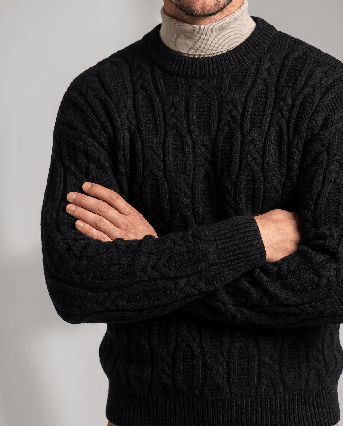 Black braided knit over beige mock neck with arms folded