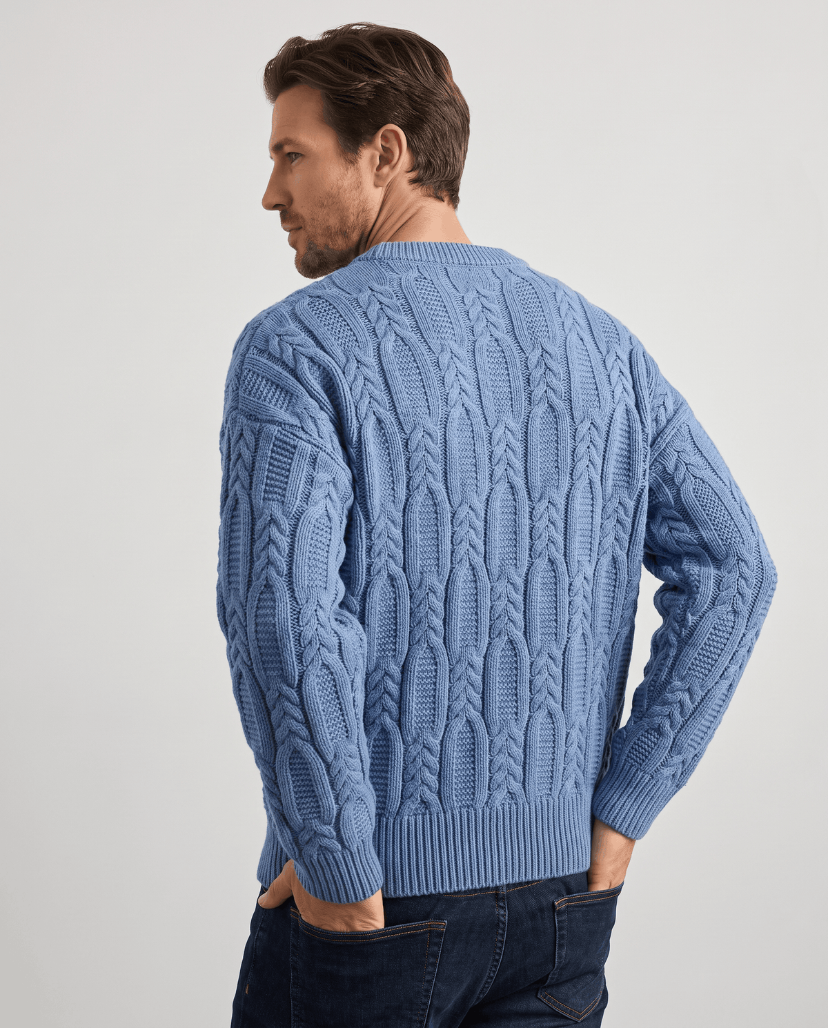Three-quarter back view of blue cable sweater with ribbed cuffs
