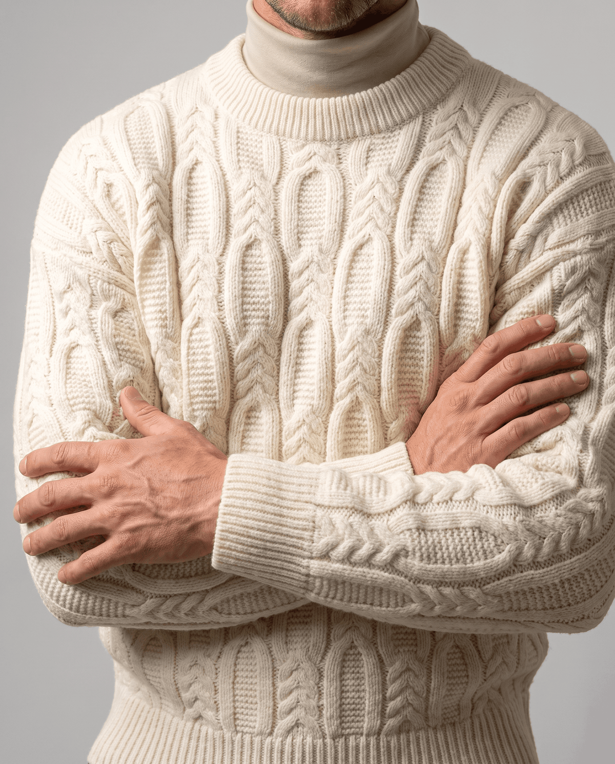 Cream braided knit worn over beige mock neck with arms crossed