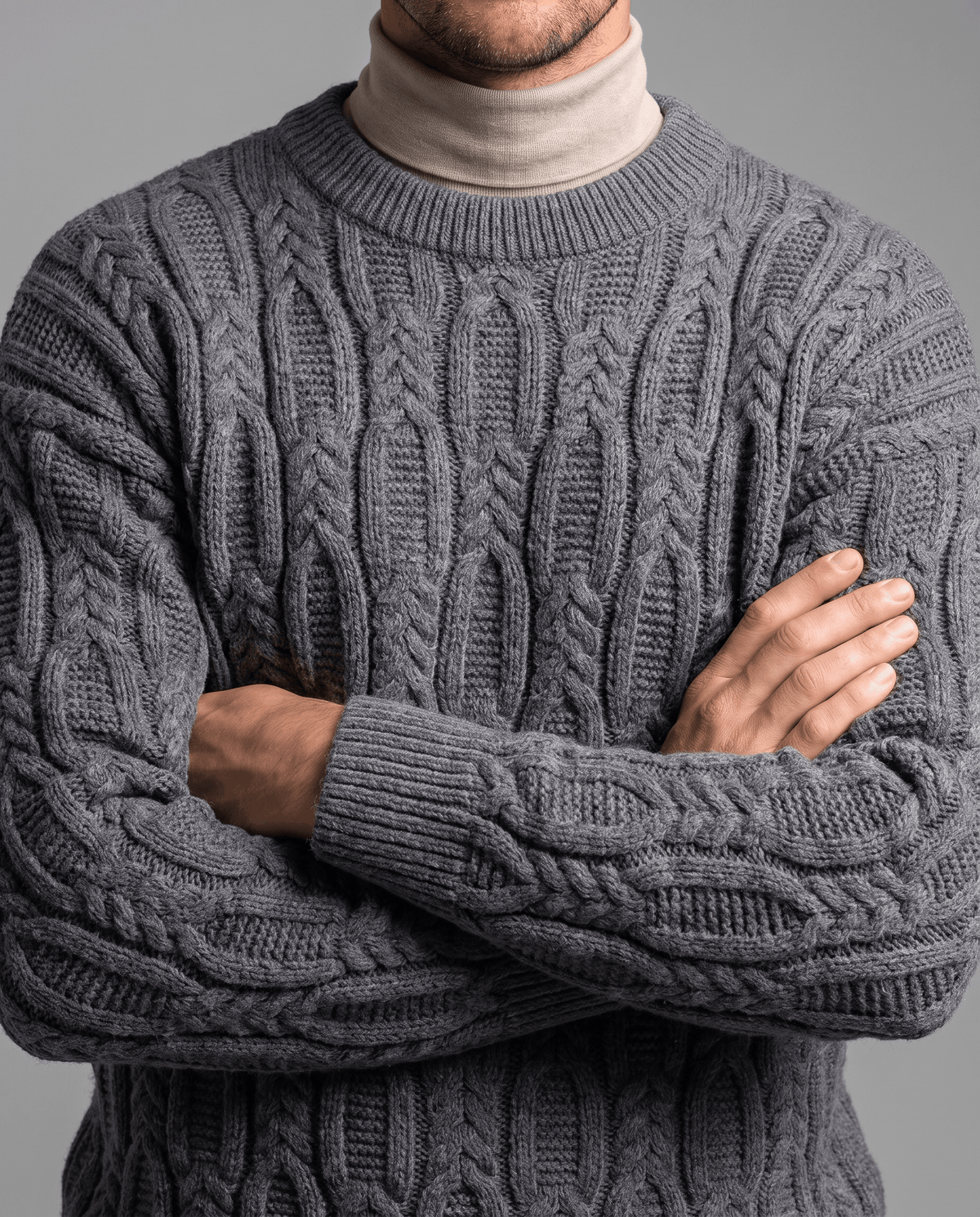 Charcoal gray braided knit over beige mock neck with arms crossed