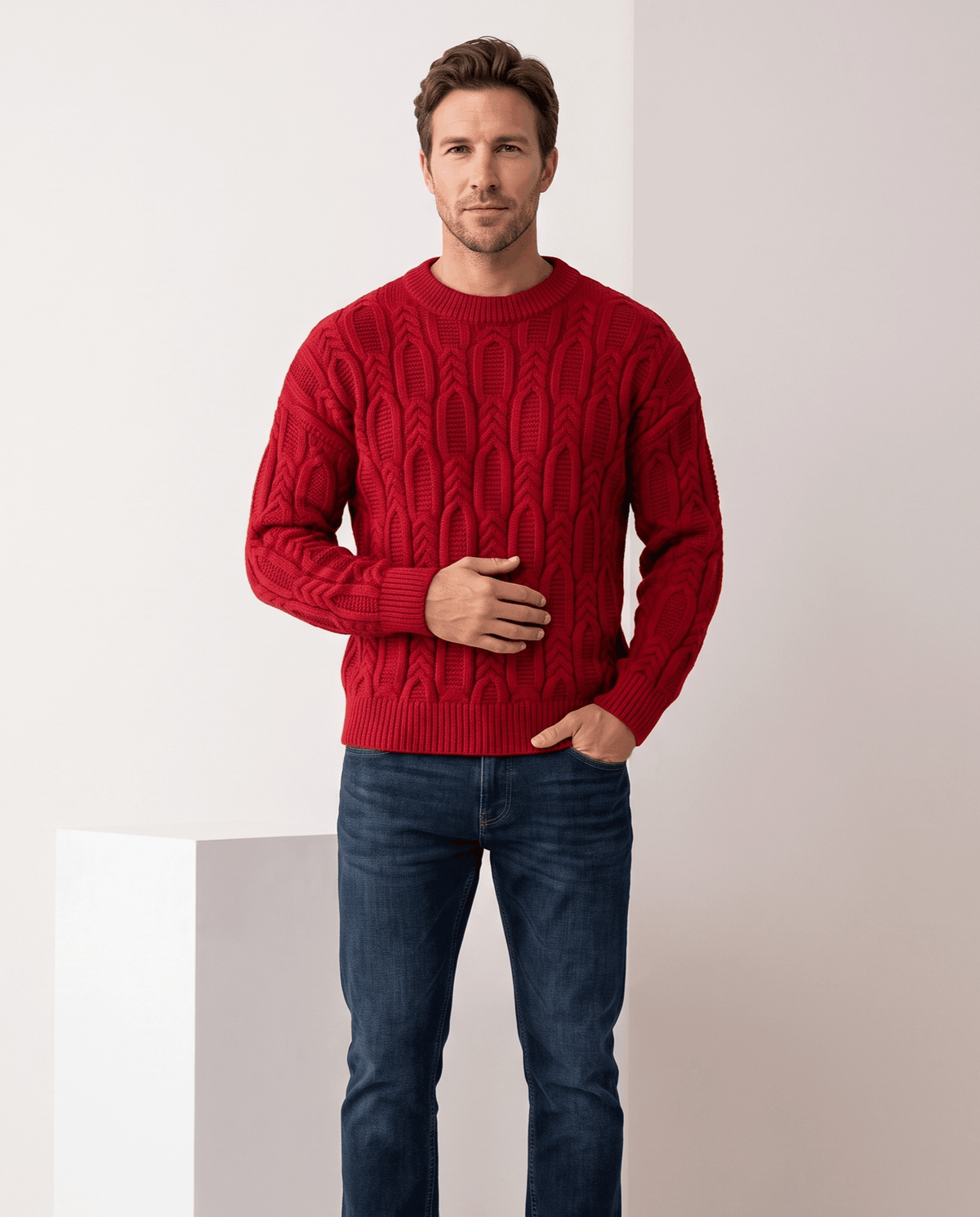 Model in red crew neck cable sweater with blue jeans beside a plinth