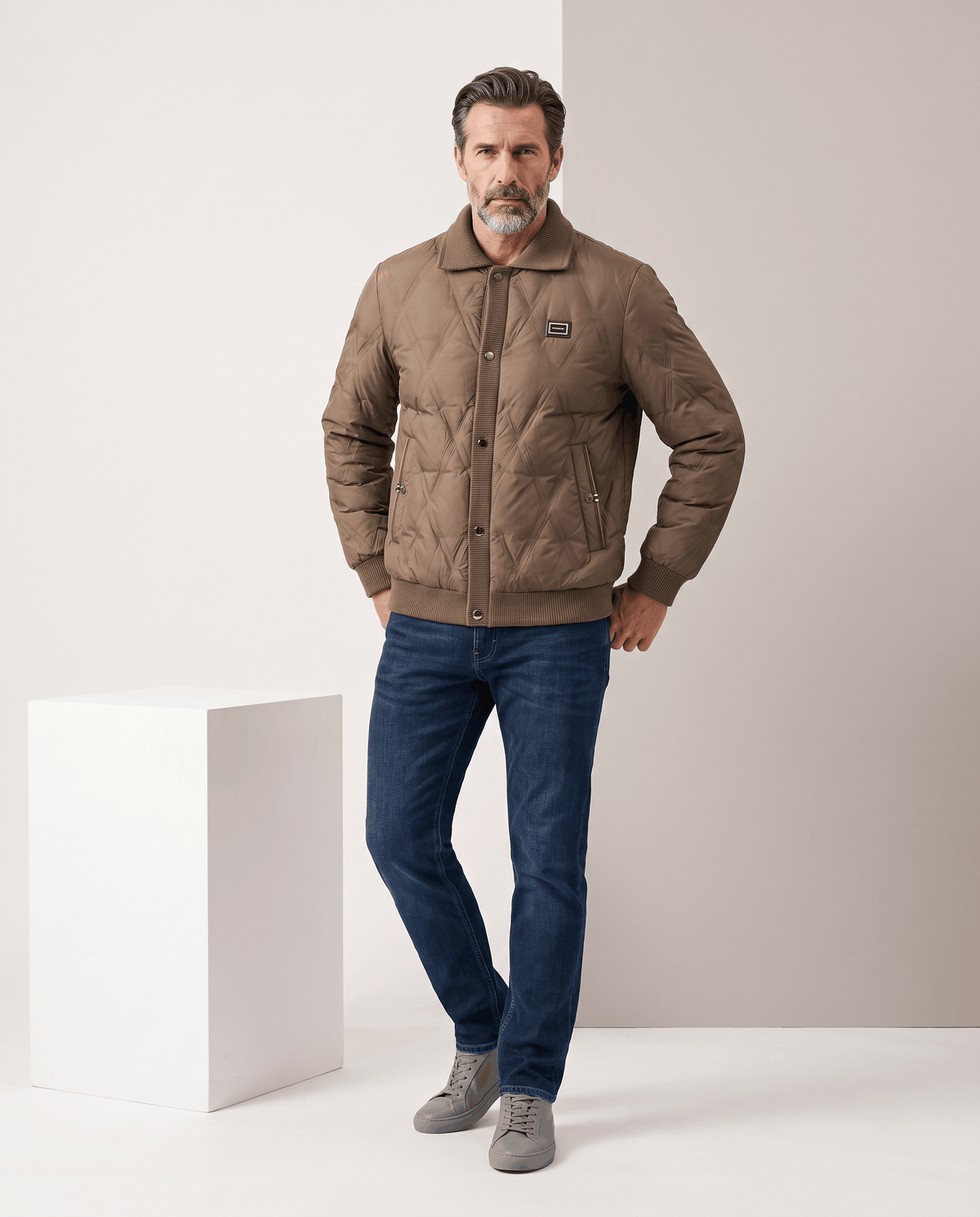 Man standing in a brown diamond quilted puffer jacket with blue jeans, full-length view