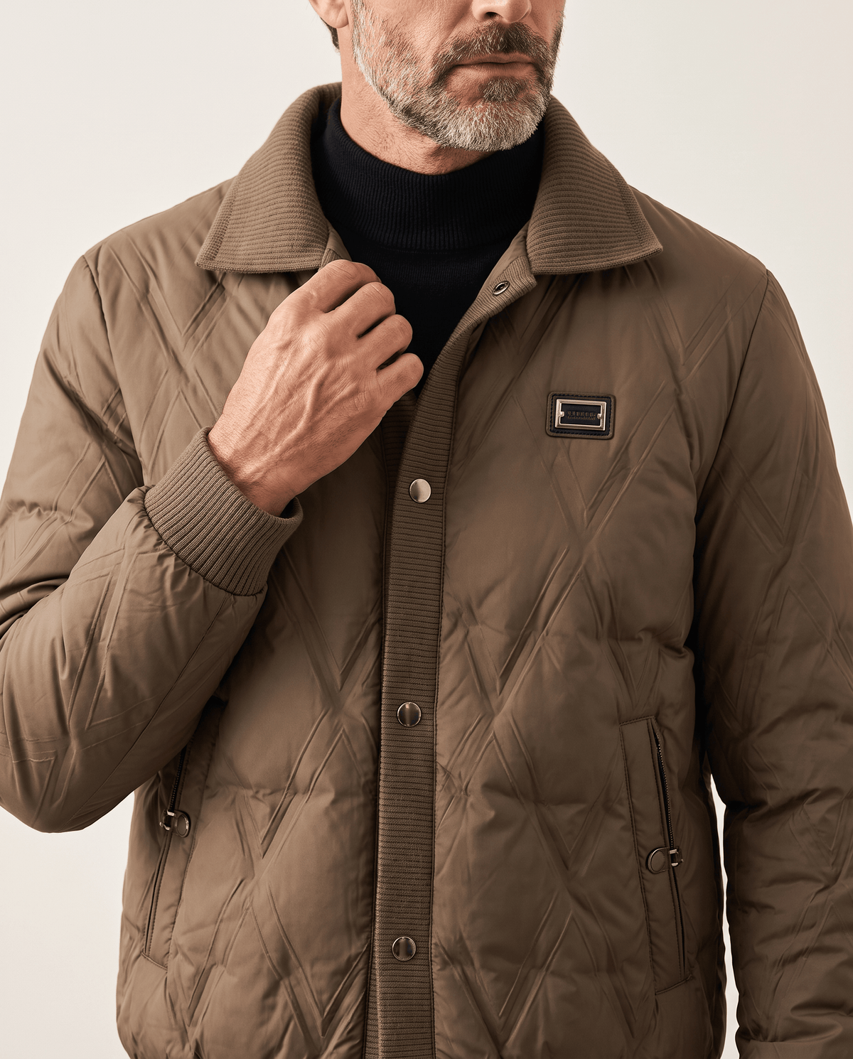Man touching the snap-button front of a brown diamond quilted puffer jacket