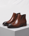 Brown Chelsea boots with darkened toe cap displayed on a gray block