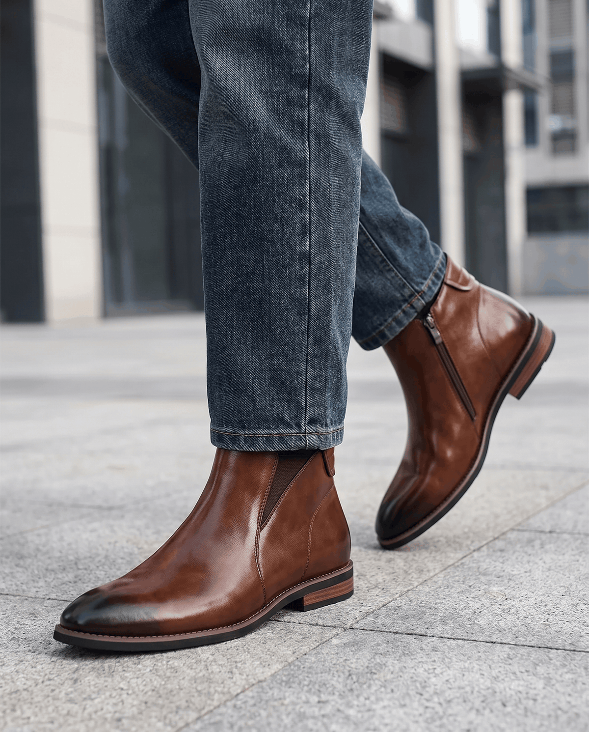 Man wearing brown Chelsea boots with blue jeans on a city pavement