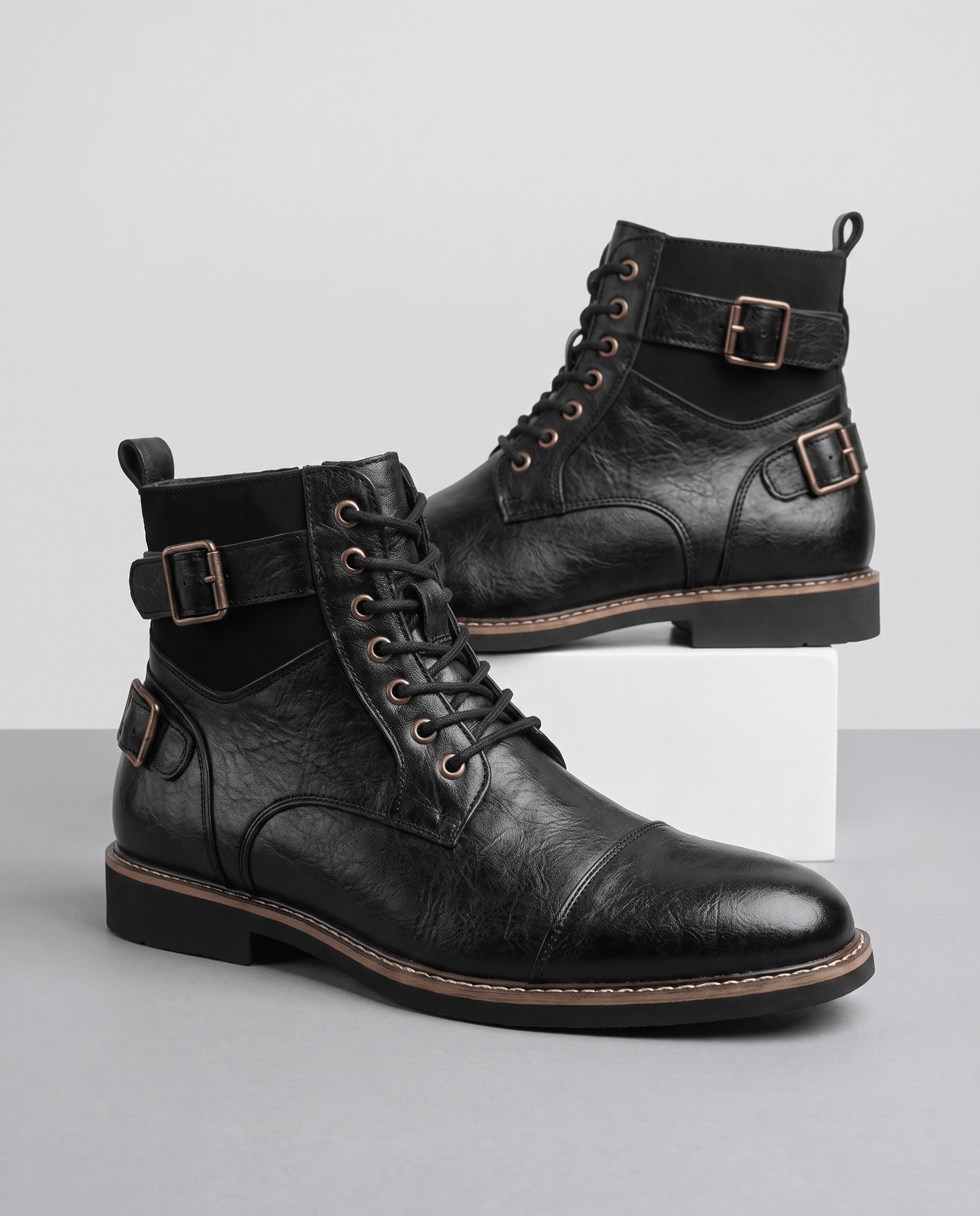 Black cap-toe lace-up boots featuring layered leather panels, adjustable buckle straps, and a stacked welted heel.