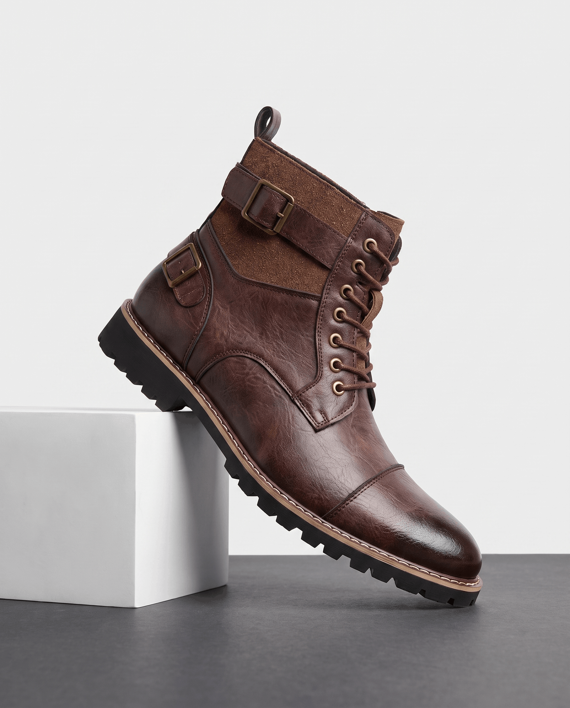 Burgundy leather cap-toe lace-up boot with suede panels, adjustable buckle strap, and a welted stacked lug sole.