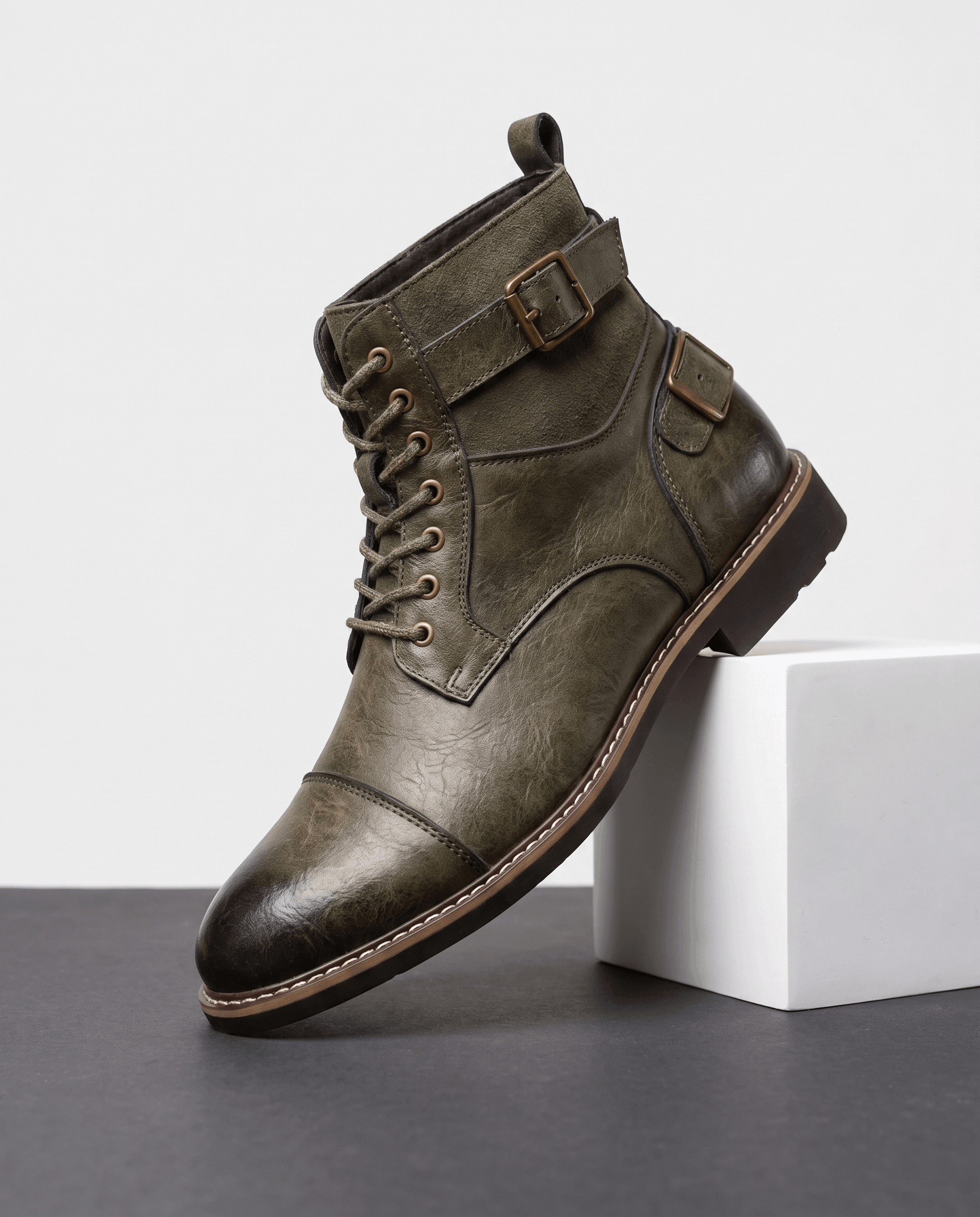 Olive green cap-toe lace-up boot with a layered leather upper, adjustable buckle strap, and a welted stacked heel.
