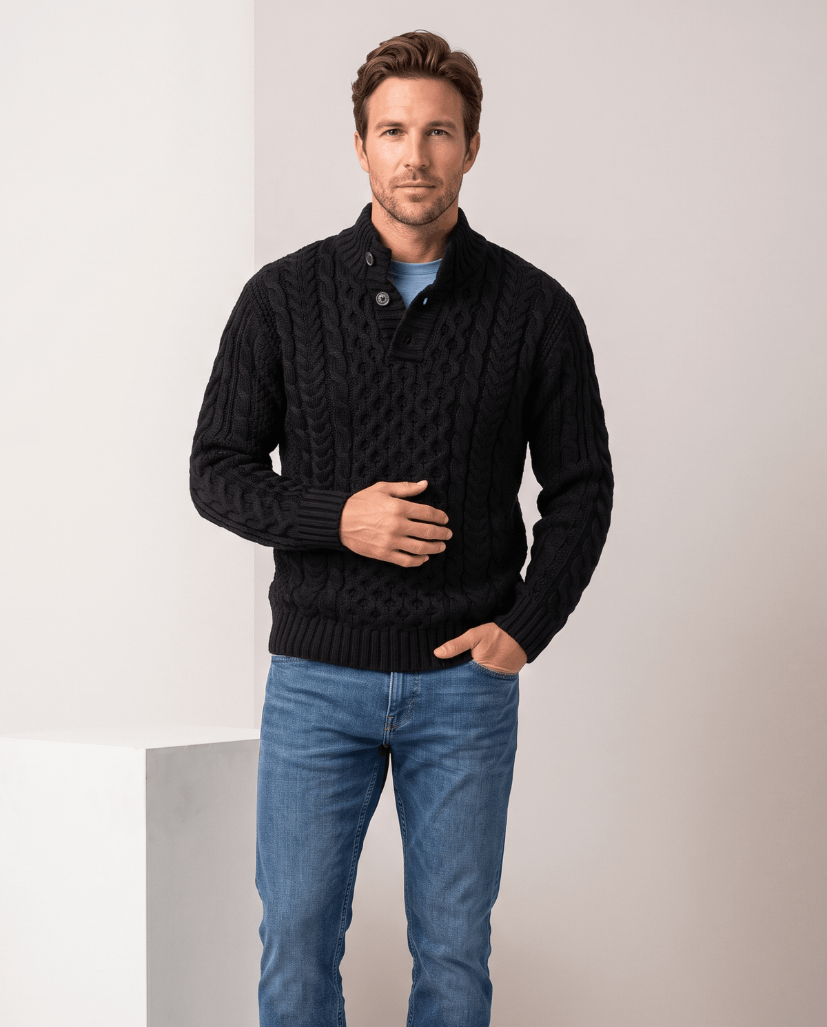 Model in black button collar cable sweater with blue jeans beside a plinth