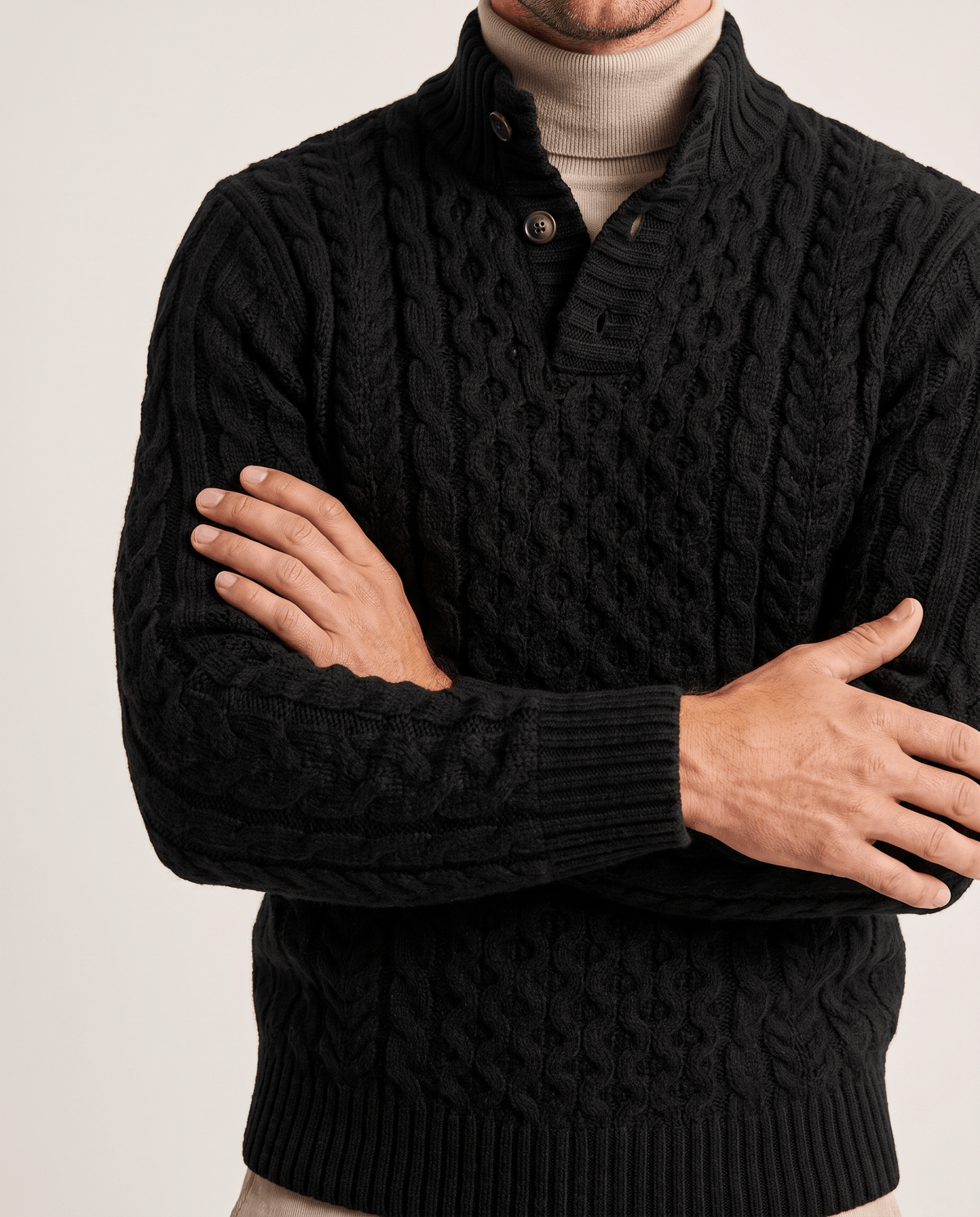 Black cable knit over beige turtleneck with arms crossed showing sleeve cables