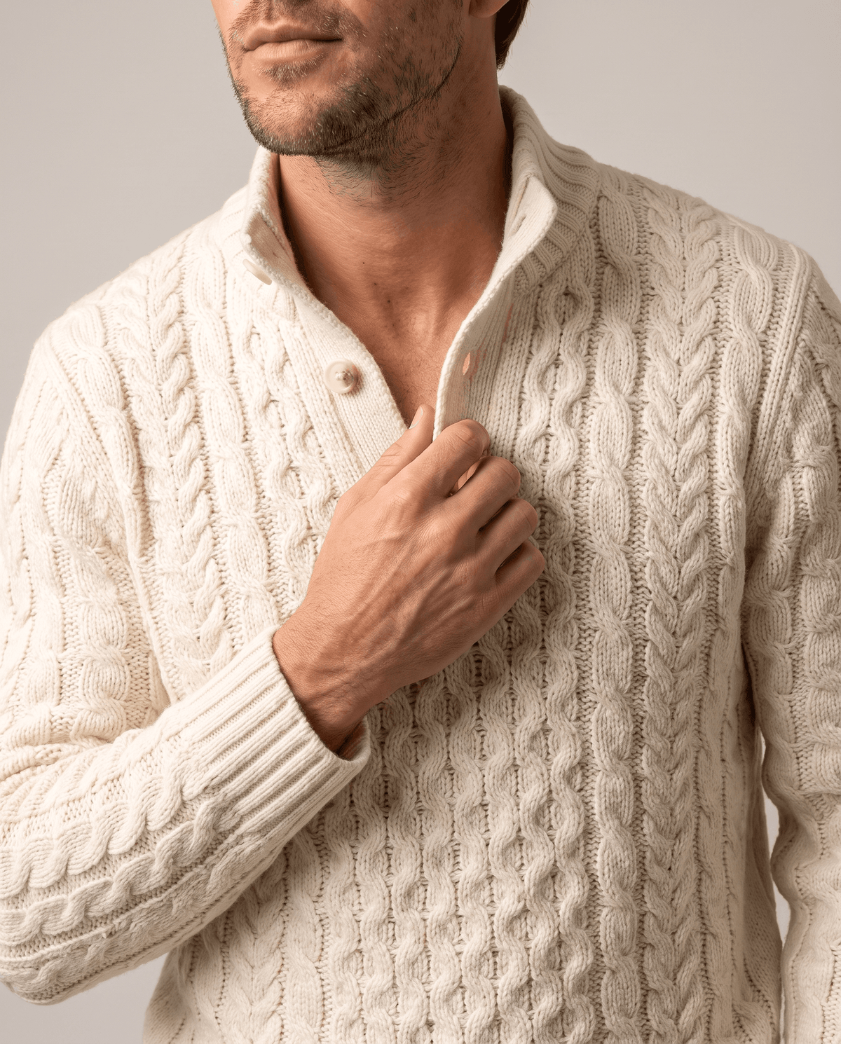 Hand adjusting the button placket of a cream cable-knit pullover