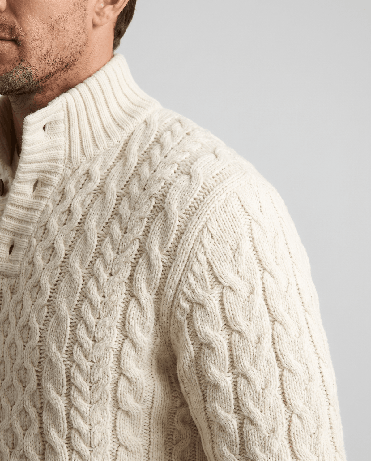 Shoulder close-up of cream sweater showing rope cables and ribbed collar