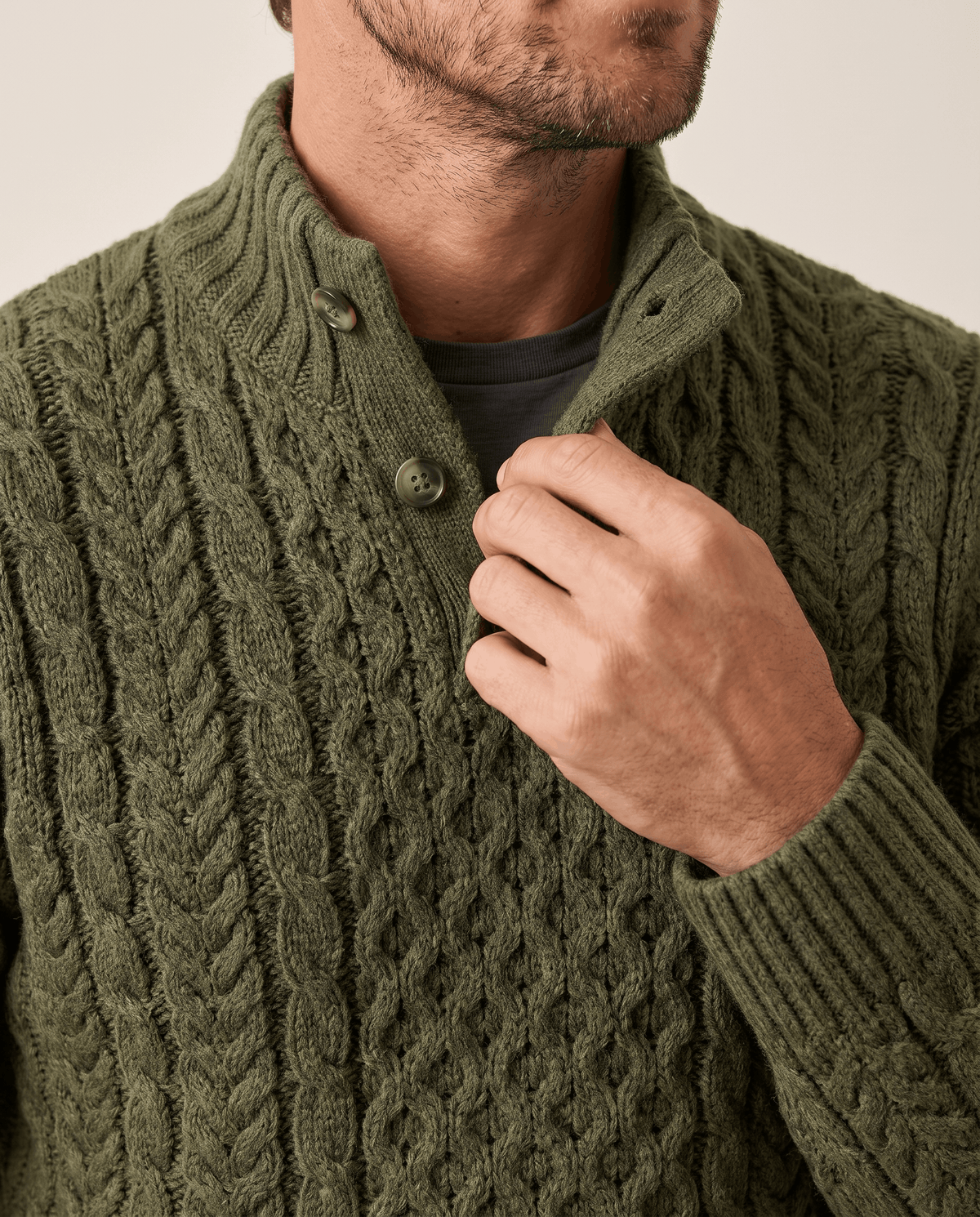 Hand at the ribbed button collar of a dark green chunky knit