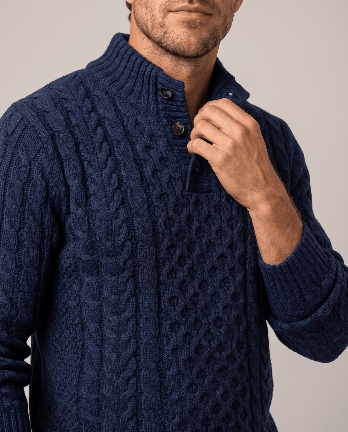 Hand at the button placket of a navy chunky cable sweater