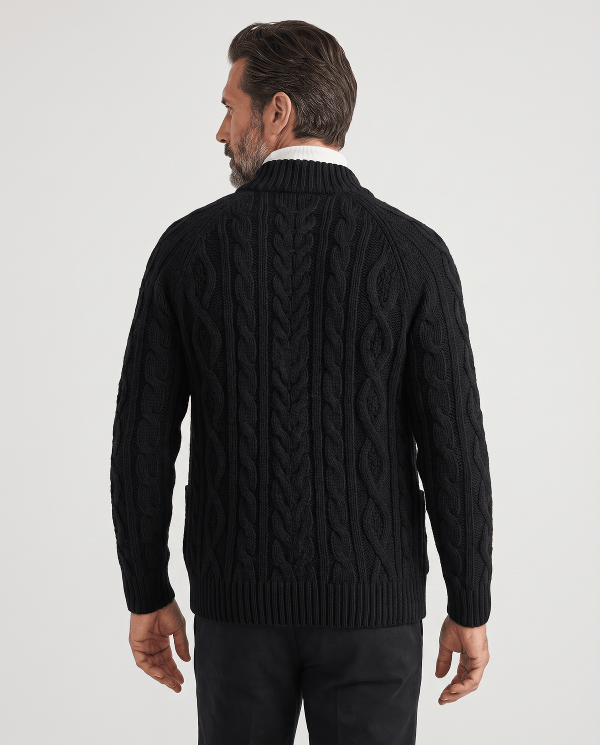 Back view of black cable knit cardigan worn with gray trousers