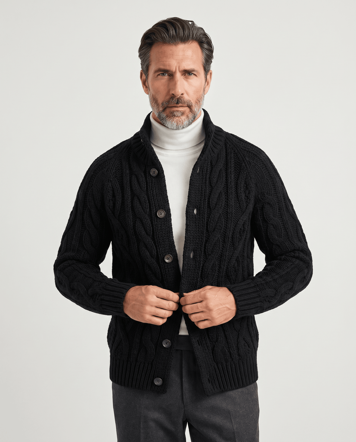 Men's black cable knit cardigan with button front worn over a white turtleneck