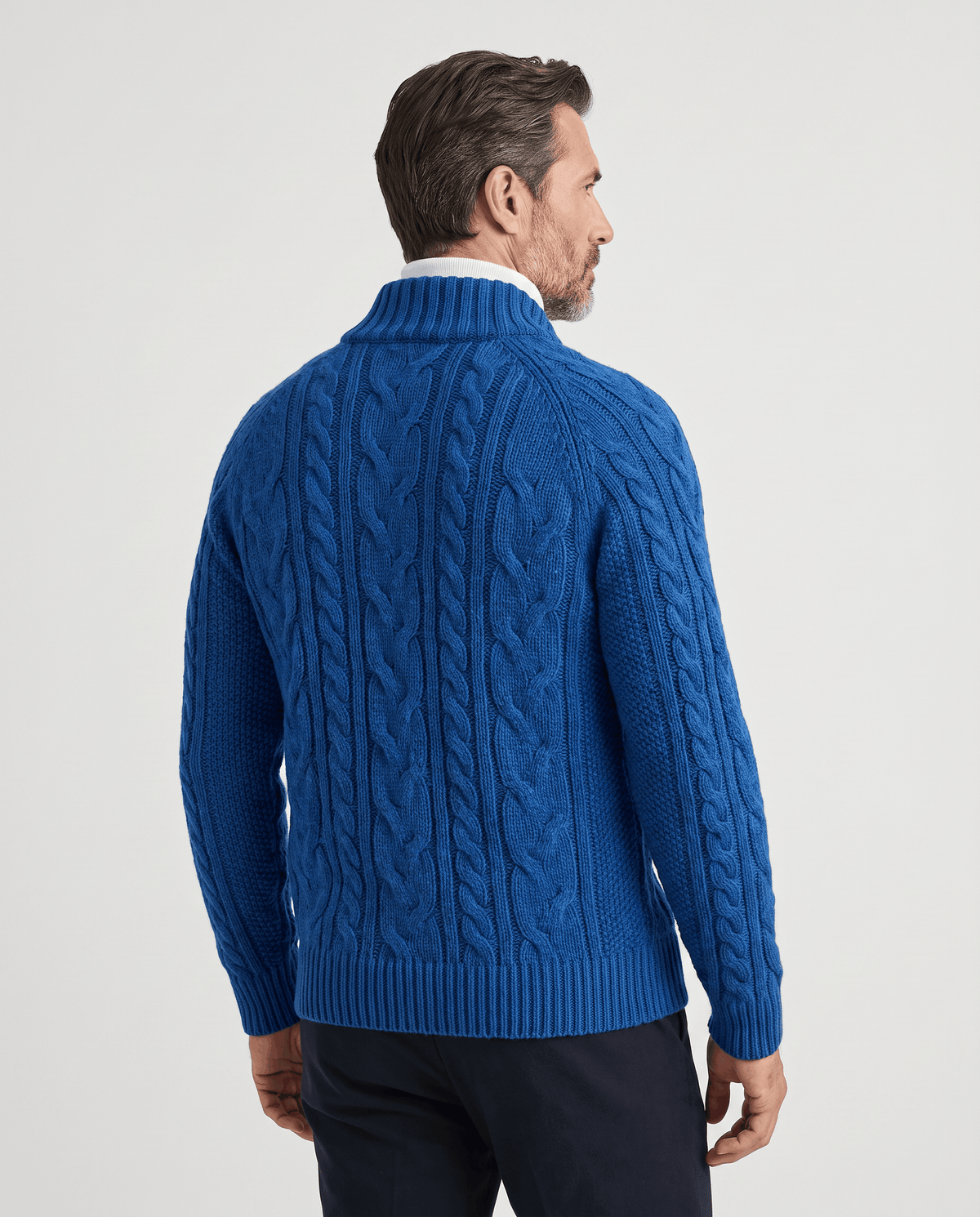 Back view of blue cable knit cardigan worn with dark trousers
