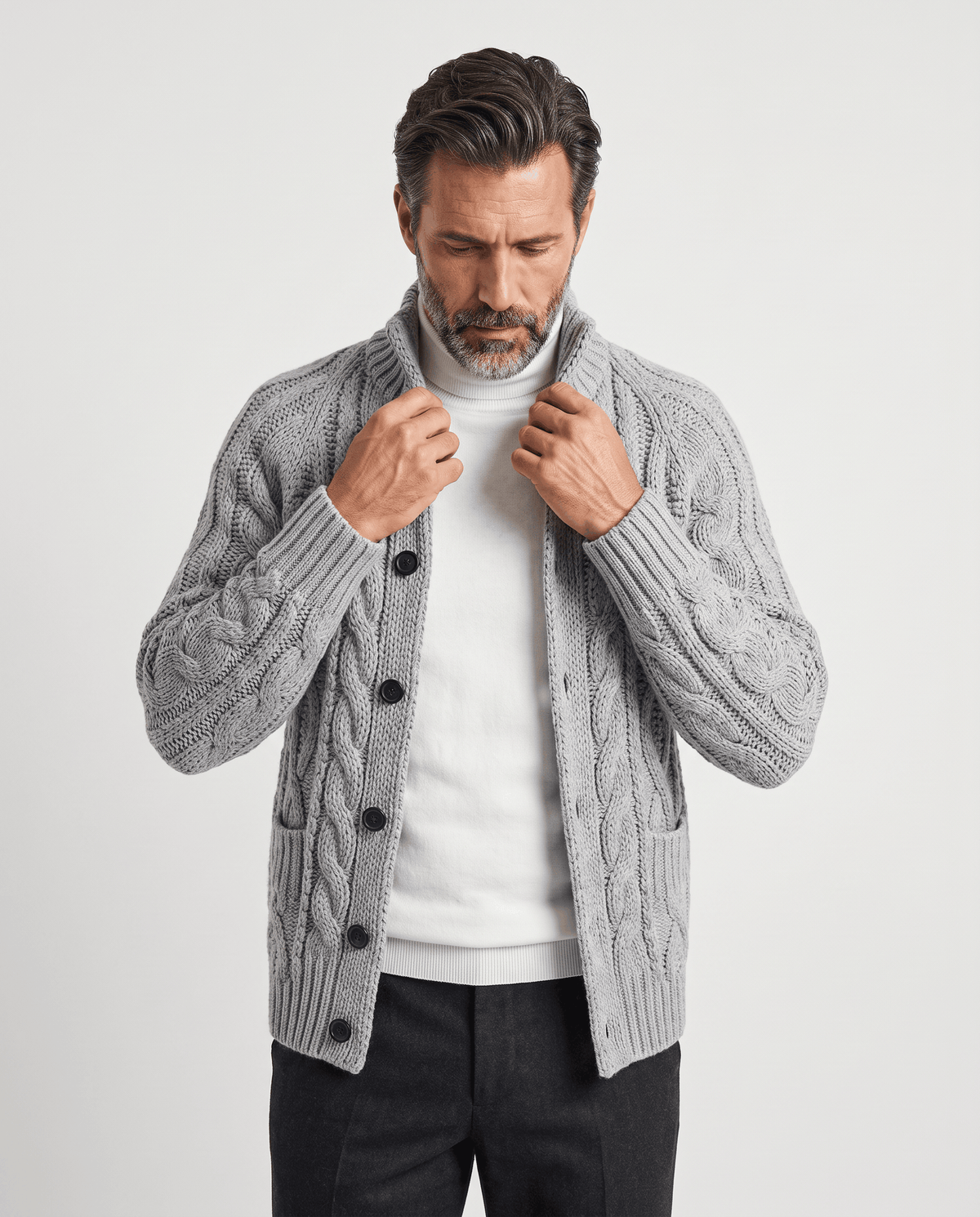 Men's gray cable knit cardigan with button front worn over a white tee