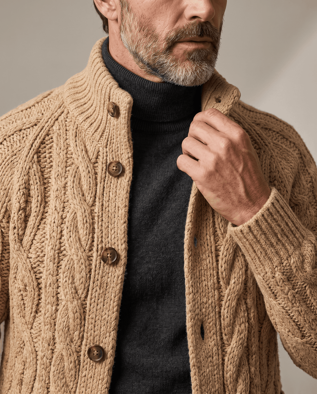 Light brown cable knit cardigan over a black turtleneck, close view