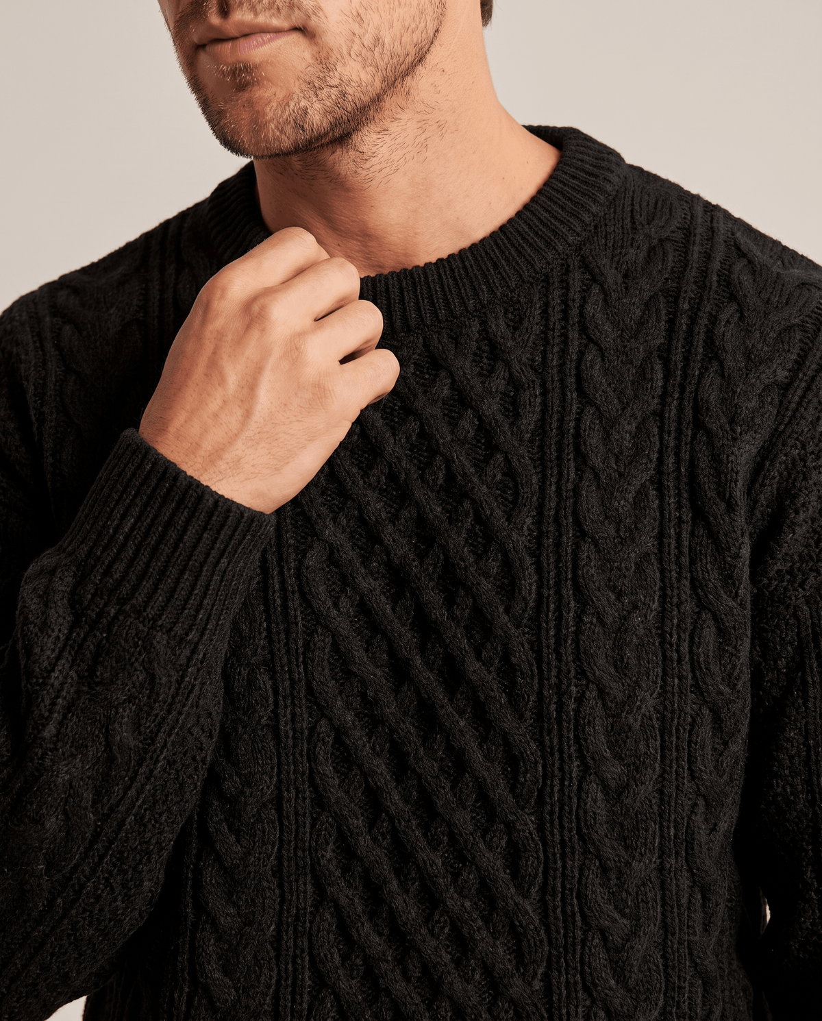 Close-up of hand at the ribbed crew collar of a black chunky knit