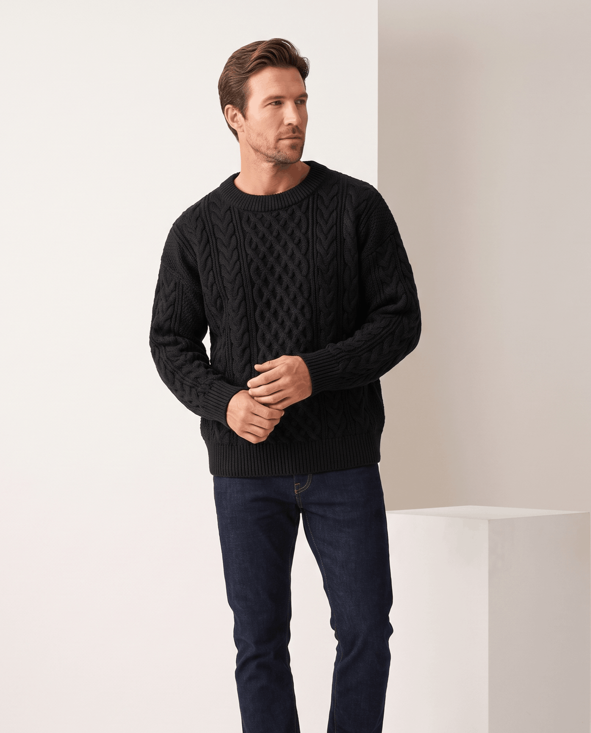 Model in black crew neck cable sweater with dark jeans and hands clasped
