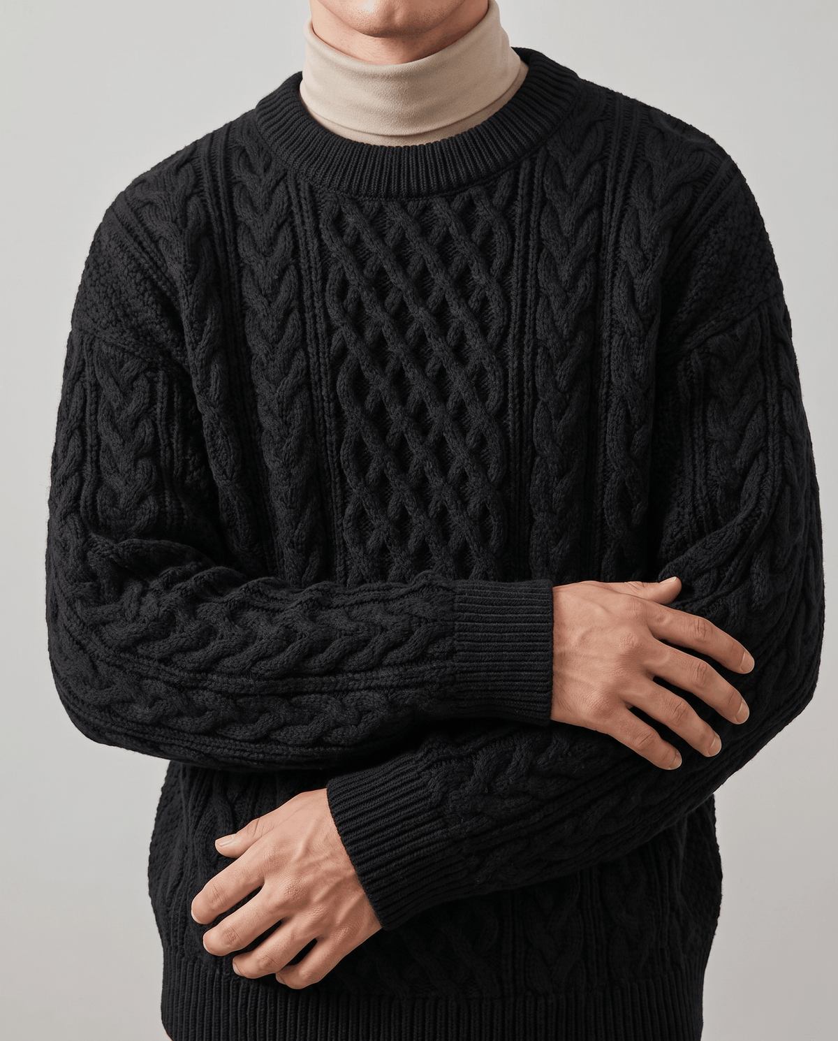 Black chunky knit over tan mock neck with arms crossed showing sleeve cables