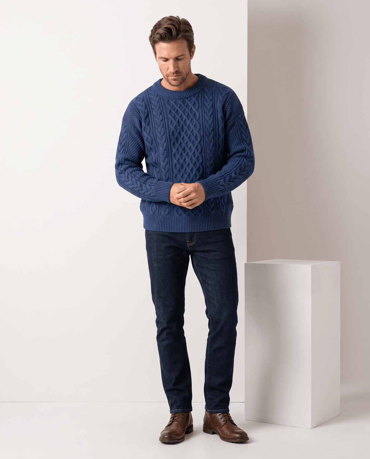 Full-length blue cable pullover worn with dark jeans and brown shoes