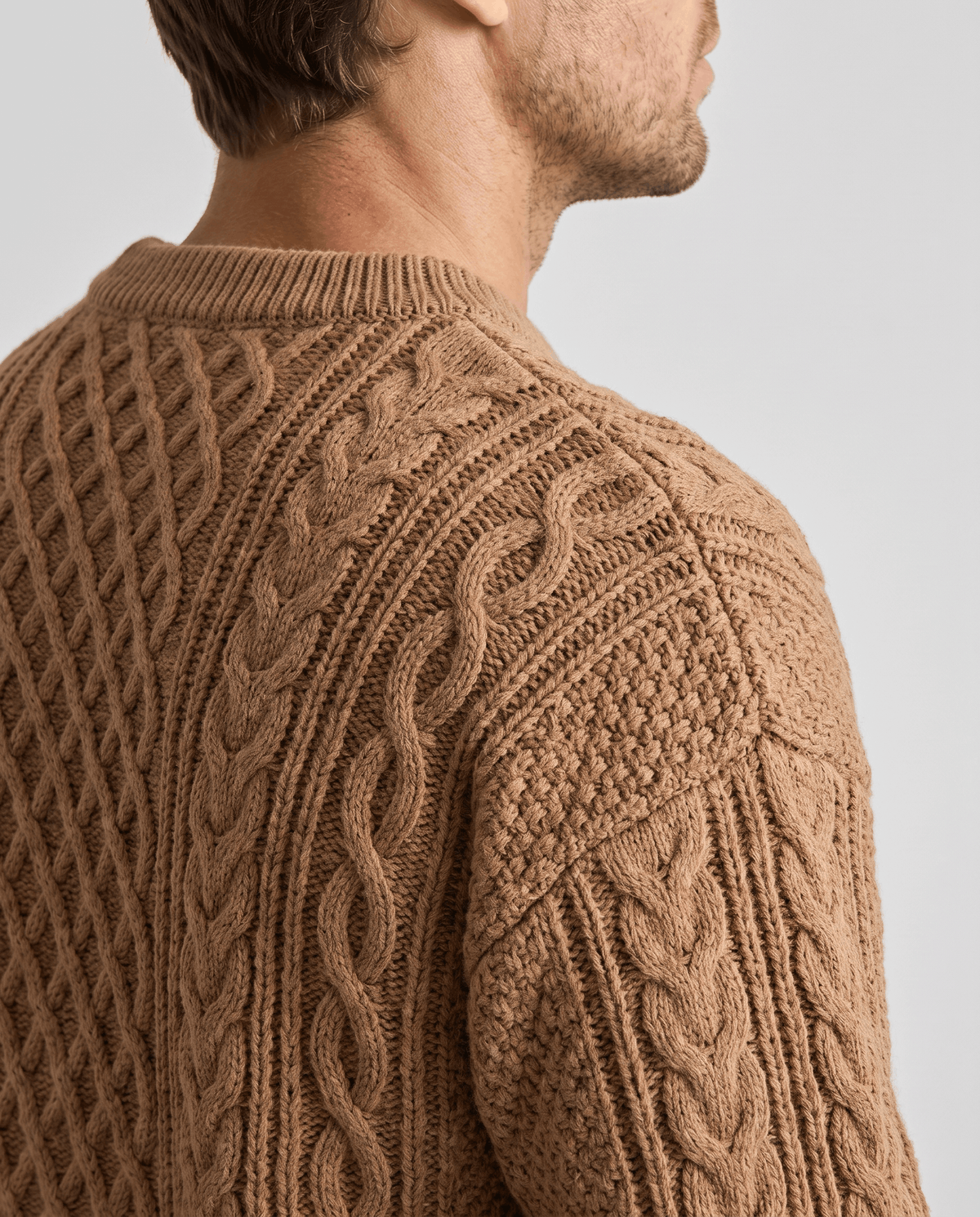 Shoulder close-up of camel sweater showing crew collar rib and rope cables