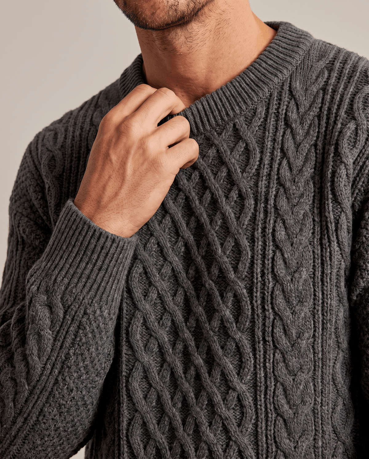 Man touching the ribbed crew collar of a charcoal gray chunky sweater