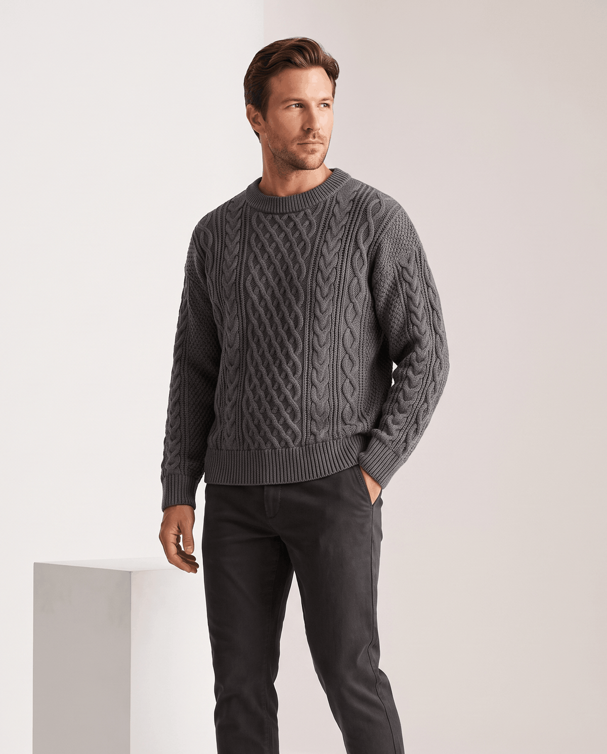 Model in charcoal gray crew neck sweater with dark trousers, hands in pockets