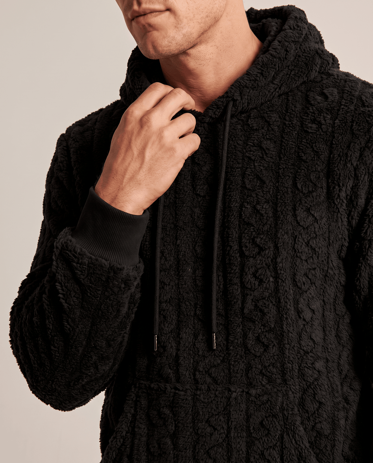 Close-up of black hoodie collar and cable pattern with a hand at the neckline