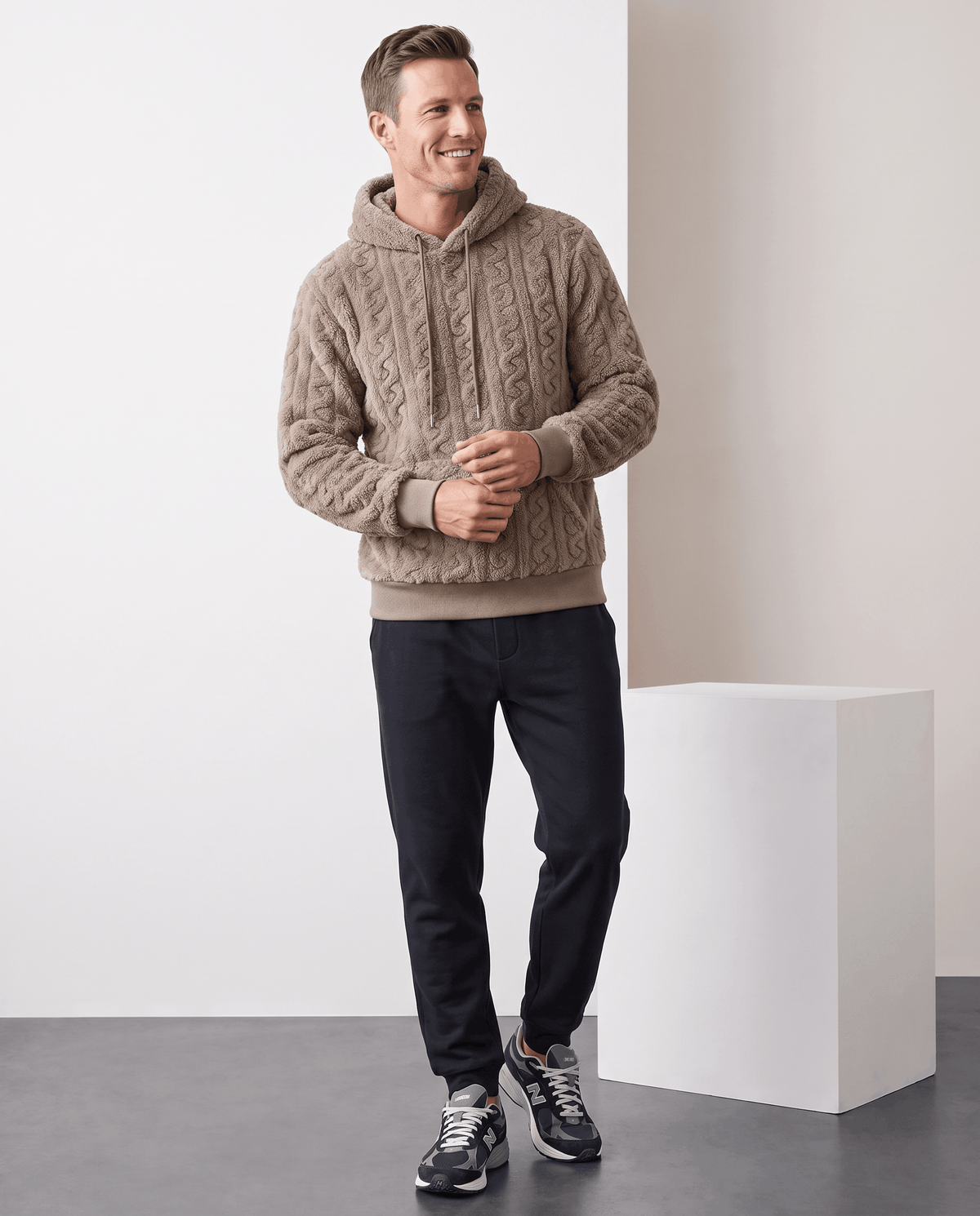 Full-length view of taupe hoodie styled with black pants and dark sneakers