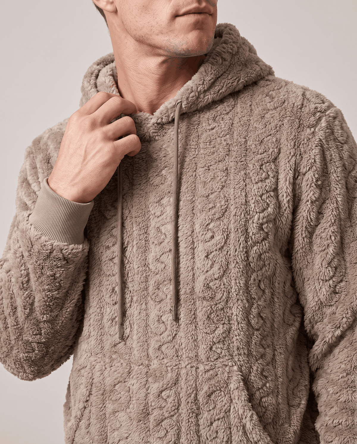 Close-up of taupe hoodie hood, drawstrings and raised cable pattern with a hand at the collar
