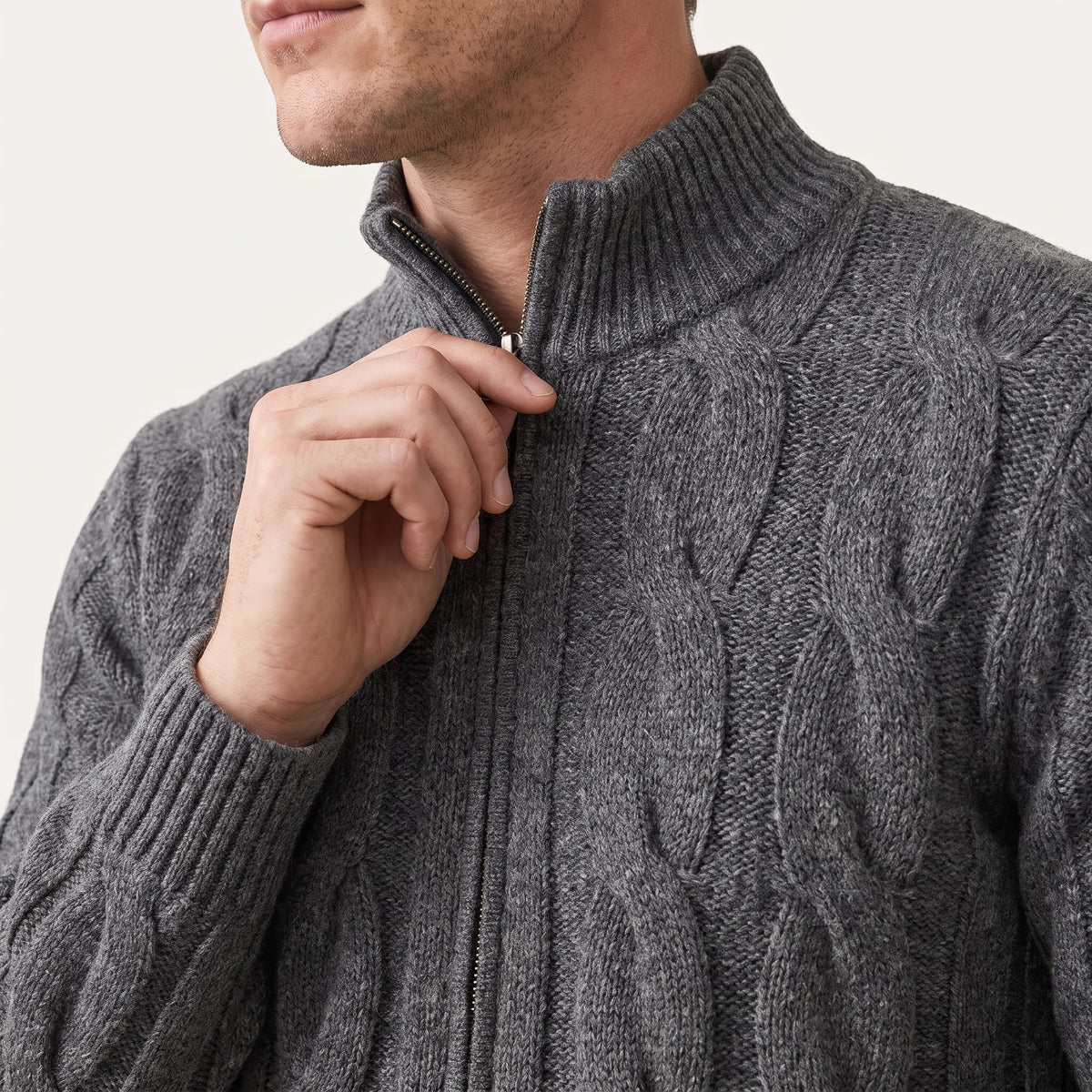 Hand at the zip and stand collar of a gray cable knit cardigan