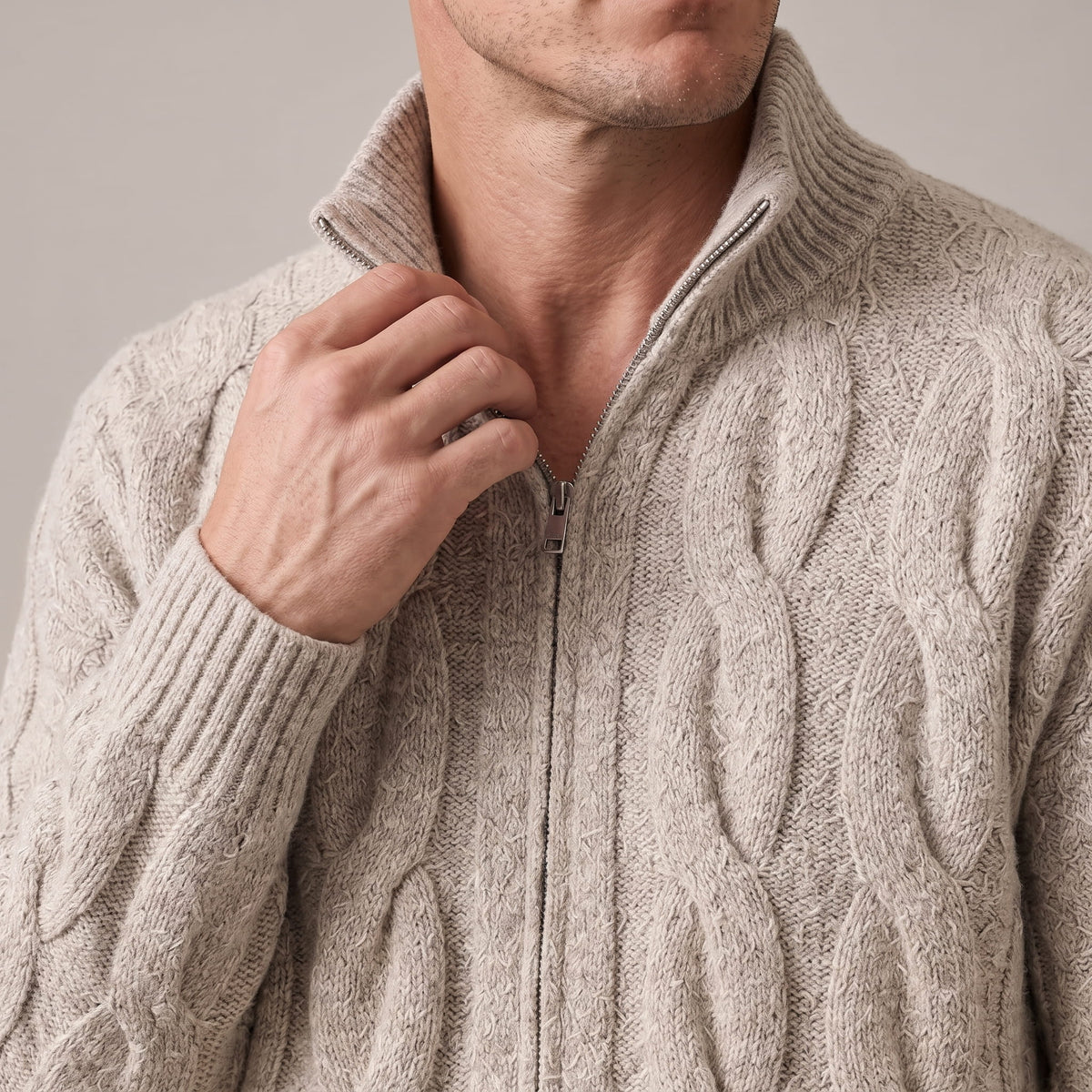 Hand at the zip of the khaki cable knit cardigan collar